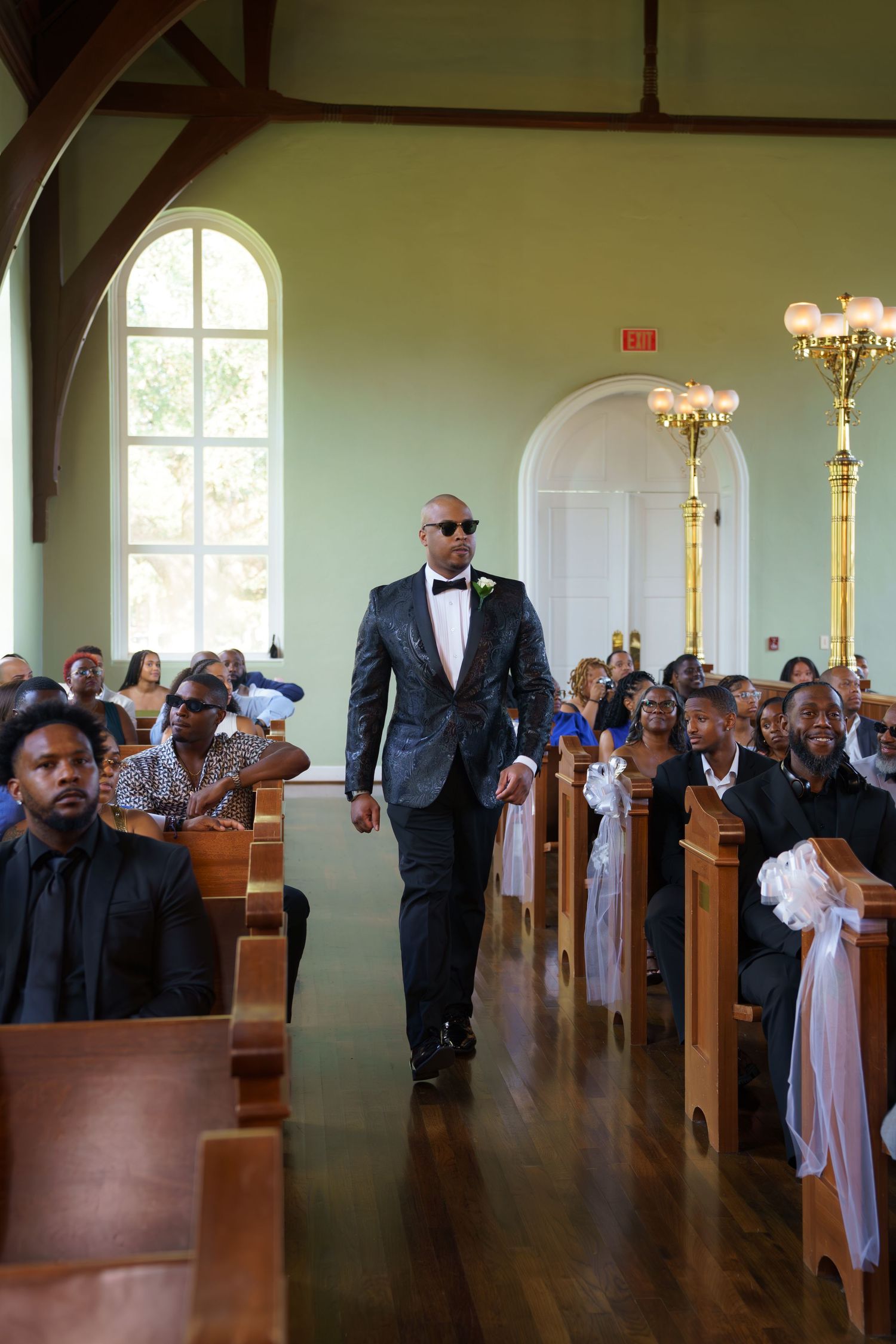 A wedding ceremony in progress inside a traditional church with wooden pews and arched windows.