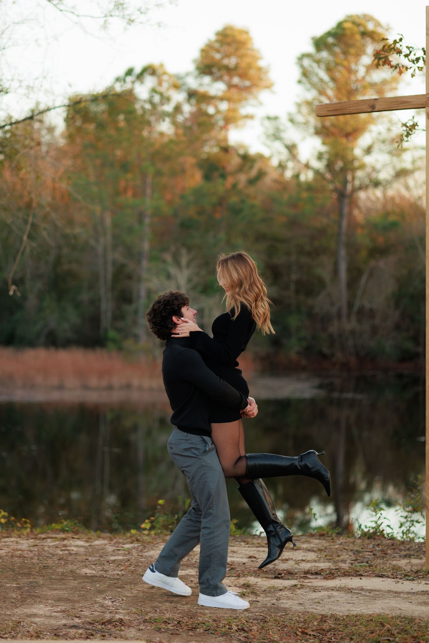 Playful moment captured between couple by a lake as one lifts the other in celebration.