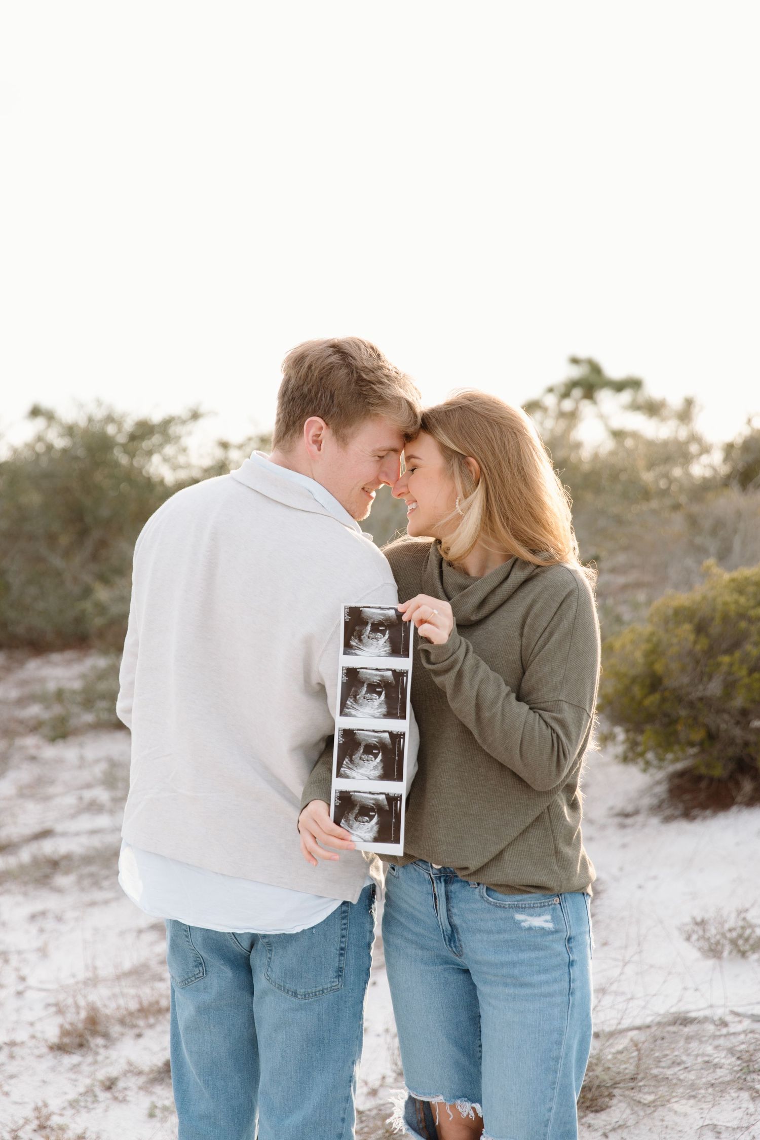 Couple sharing intimate moment while holding ultrasound photos against snowy background.
