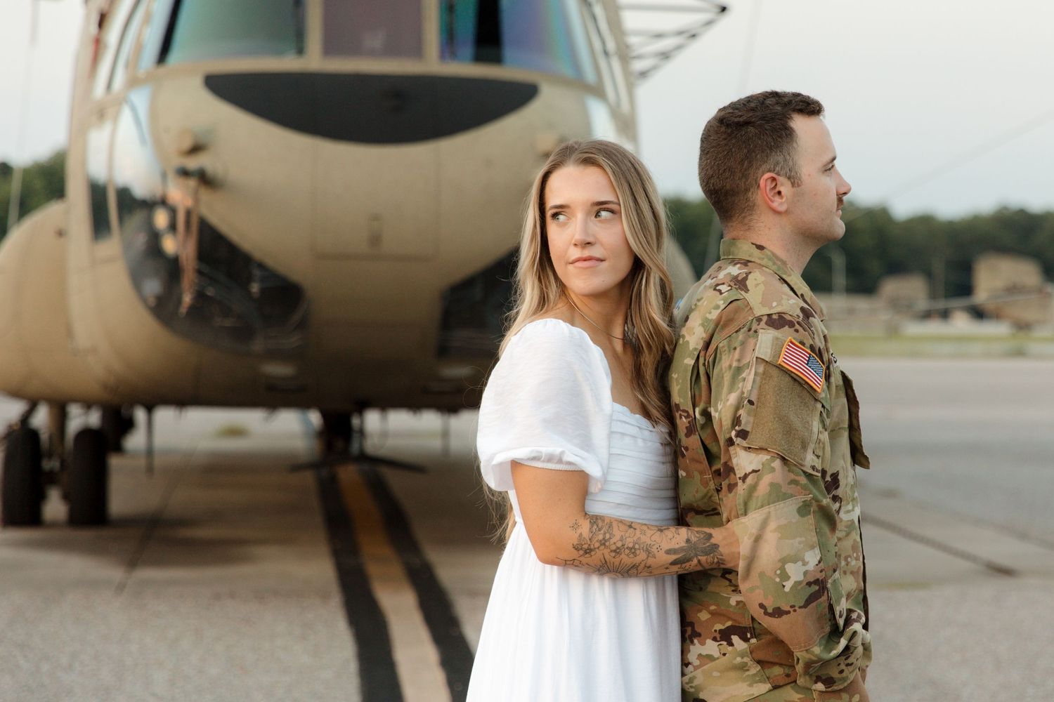 Military service member and person in white dress stand by helicopter on airfield.
