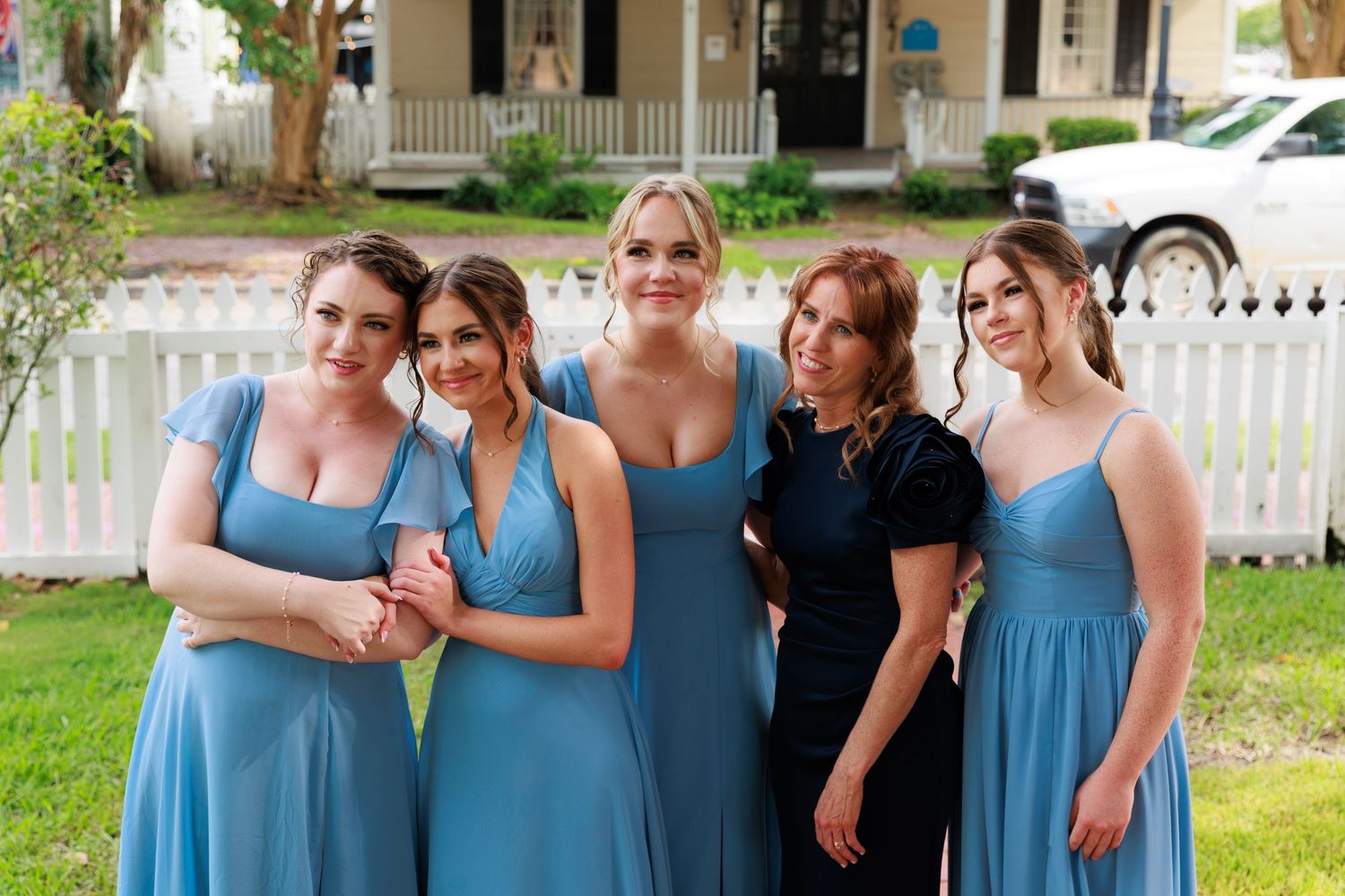 Bridesmaids in light blue dresses pose with woman in black dress outdoors.