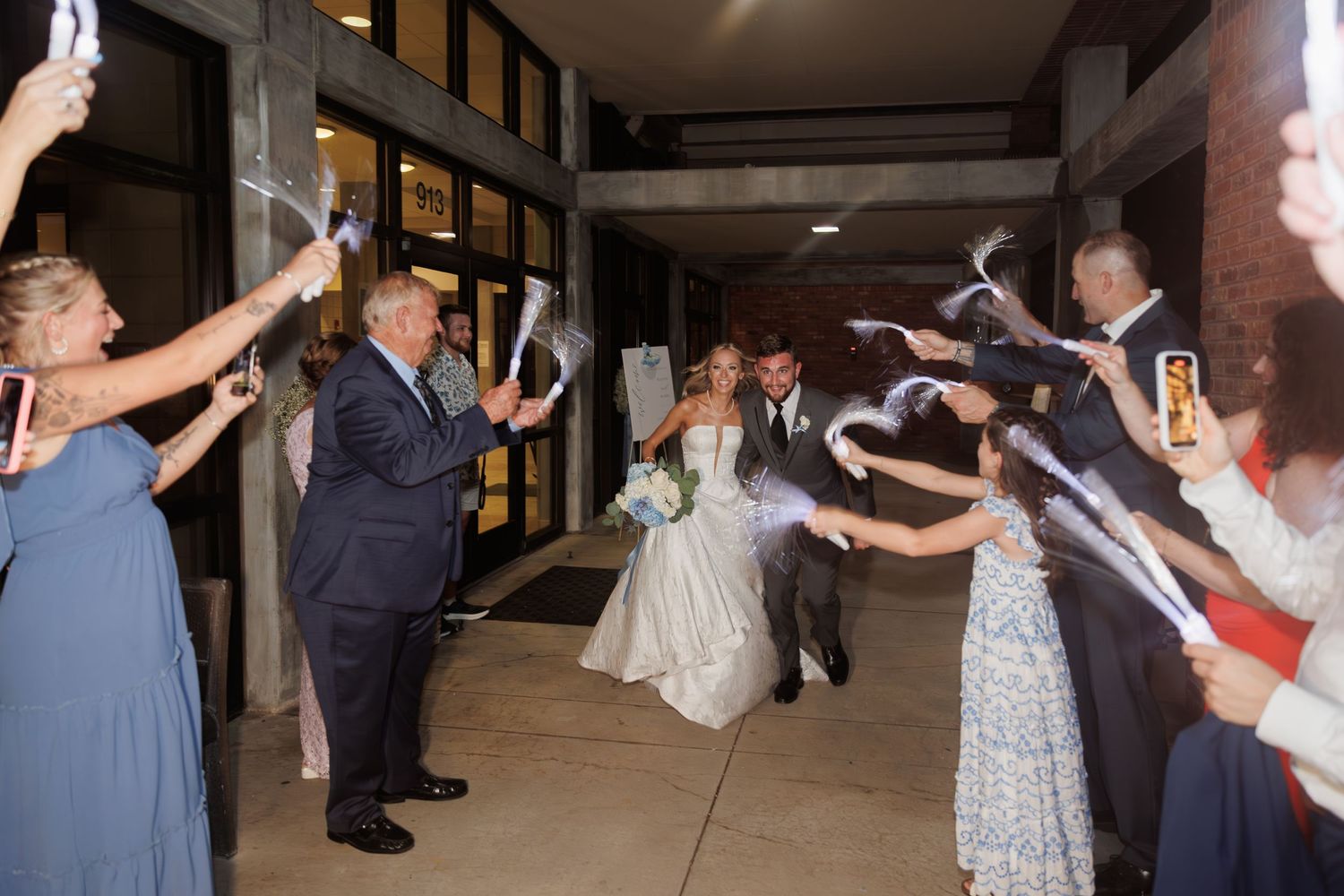 Wedding guests line walkway holding sparklers as couple makes grand exit.