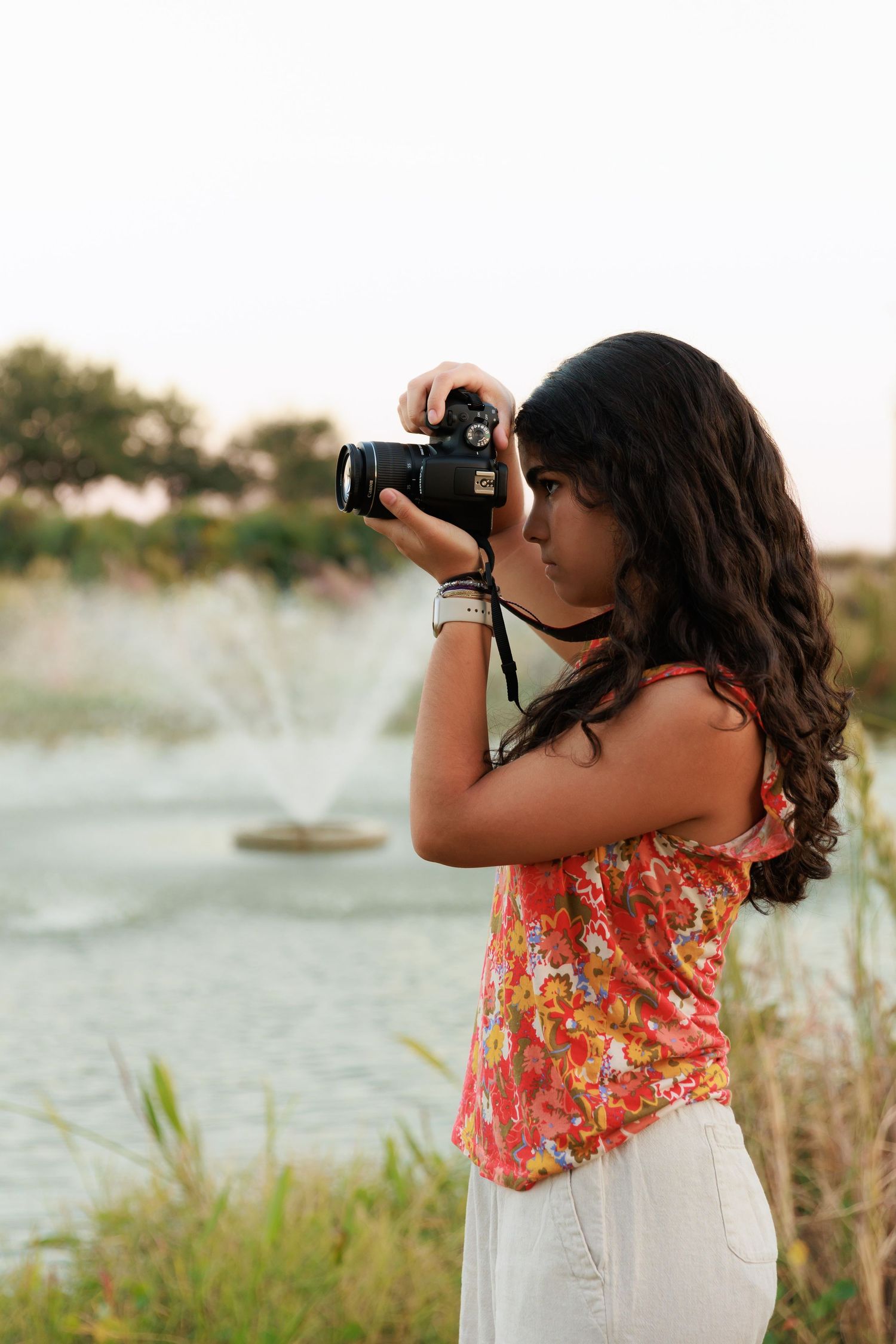 Photographer takes pictures of fountain spray while wearing orange floral top and white pants.