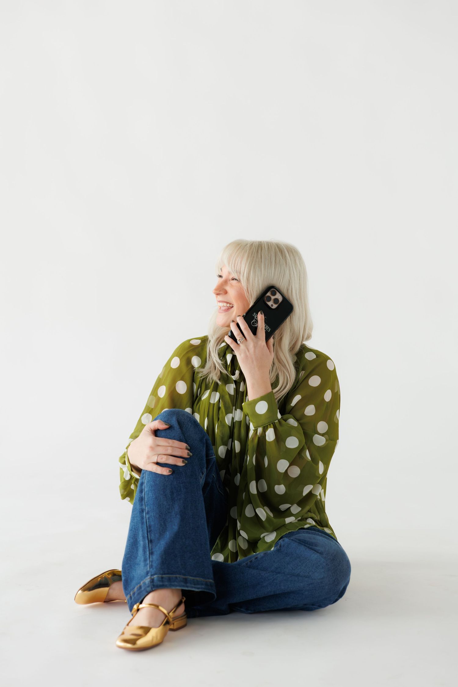 Person in polka dot top and jeans sitting on white floor in casual relaxed poses.