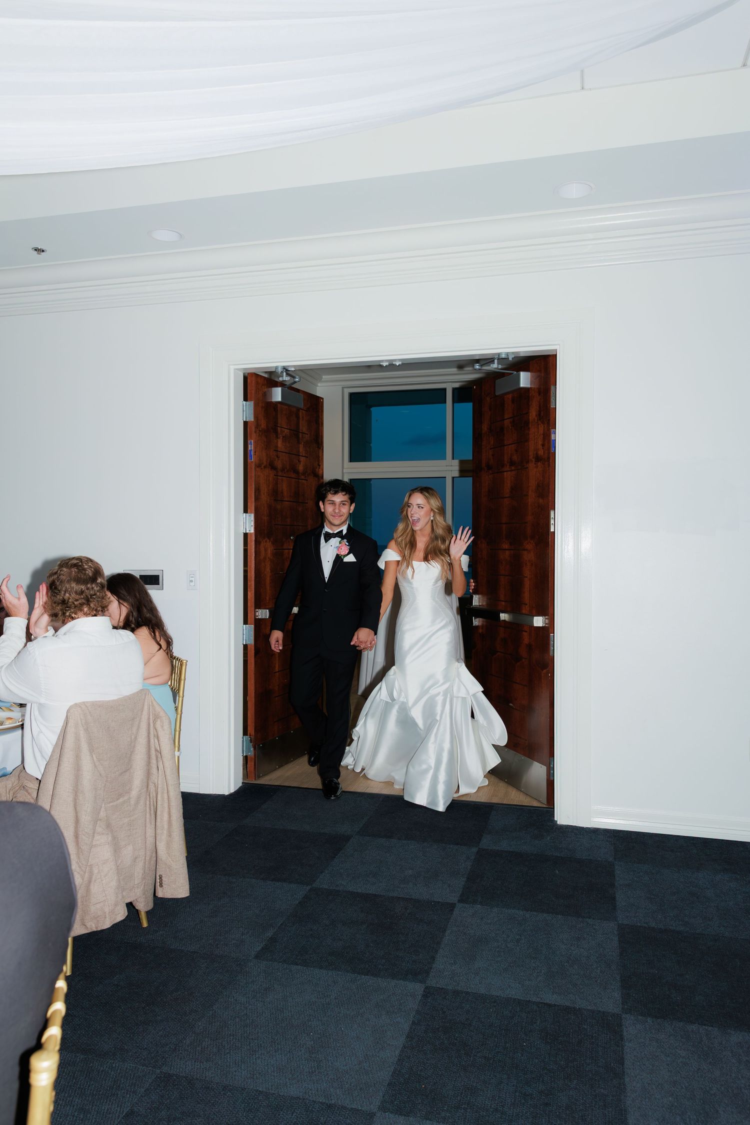 Newlyweds make their grand entrance through wooden double doors at wedding reception.