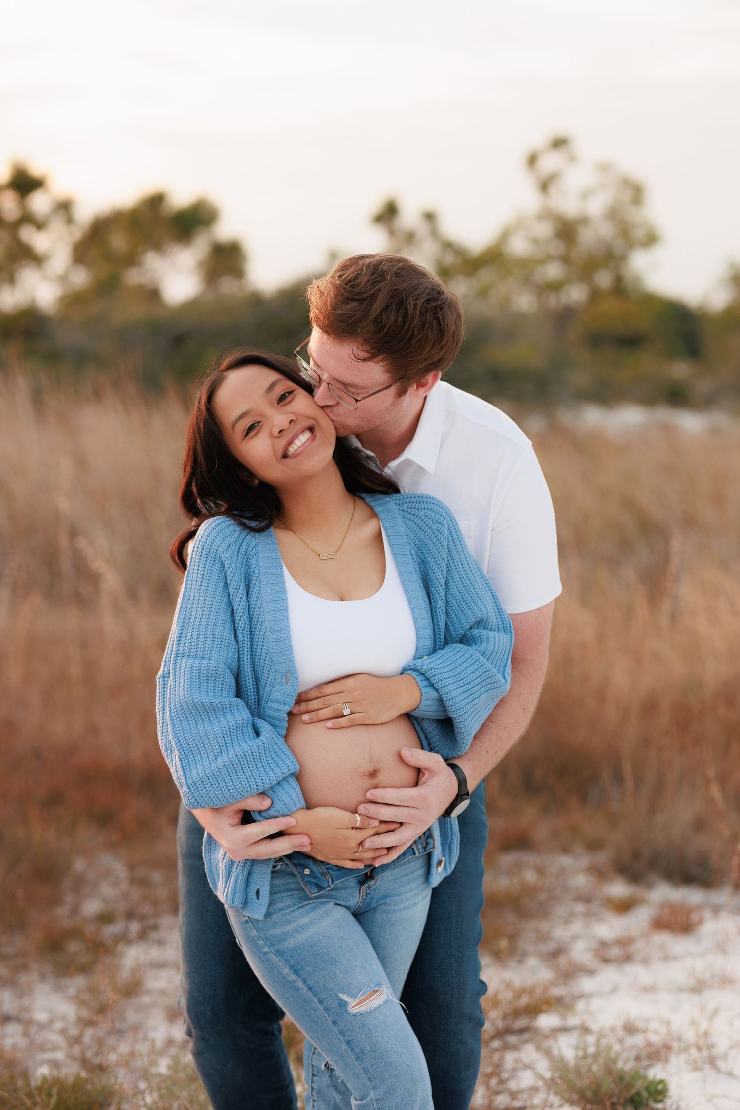 Expecting couple embraces in a field at sunset as they celebrate their pregnancy with a maternity photoshoot.