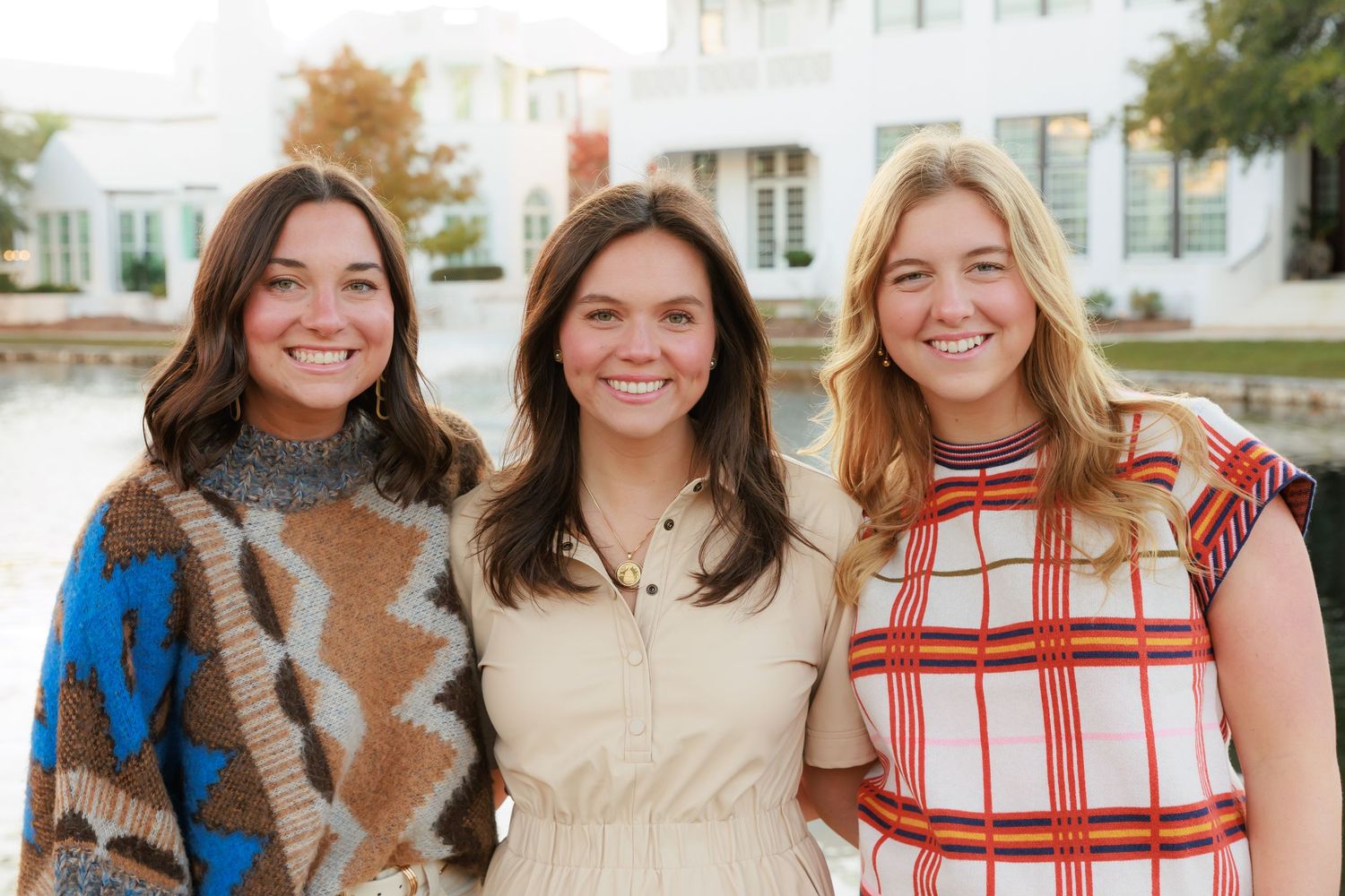 Group wearing fall colors poses together outdoors near white building.