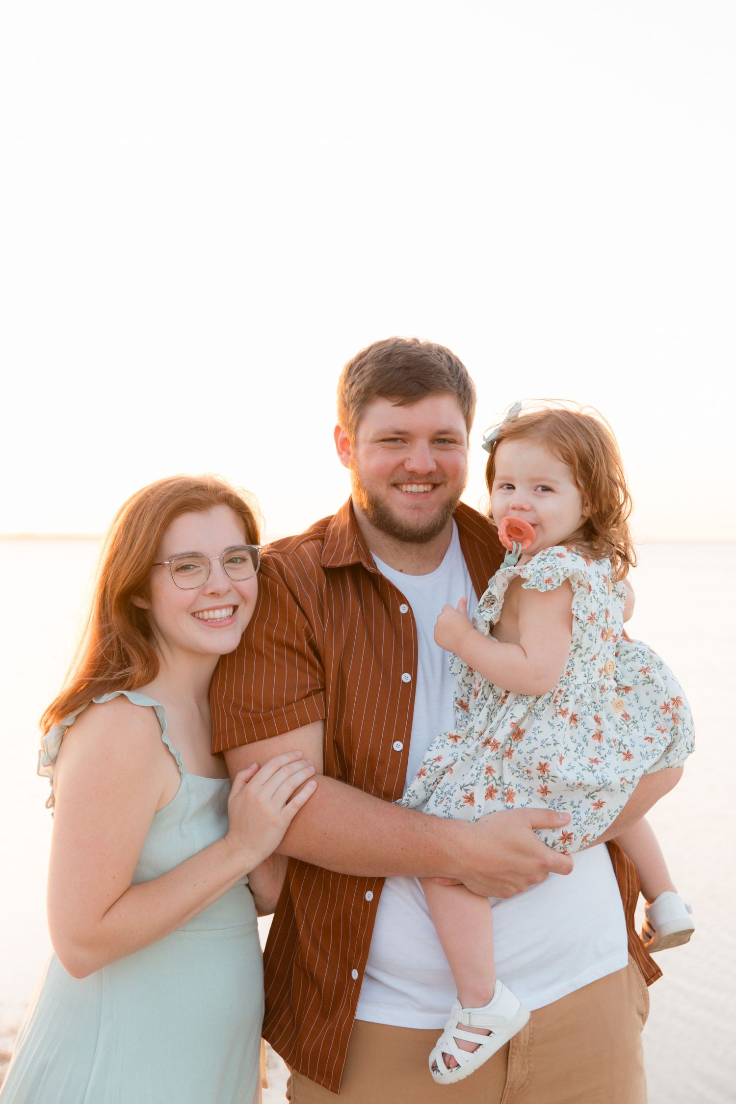 A casual outdoor family photoshoot at golden hour with warm sunset lighting and soft expressions.