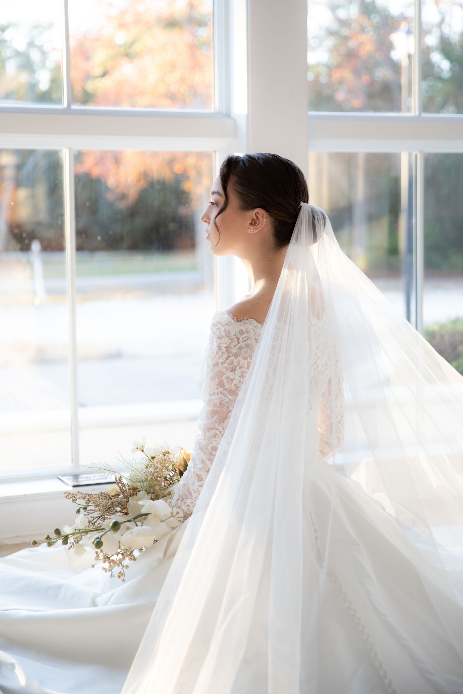 Dreamy bridal portraits in a light-filled room with autumn colors visible through windows.