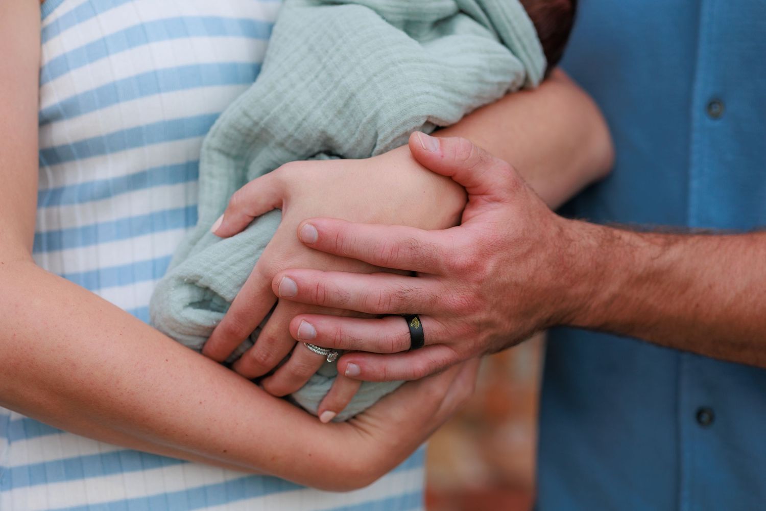 Close-up of two people holding hands together showing wedding rings against blue and striped clothing.