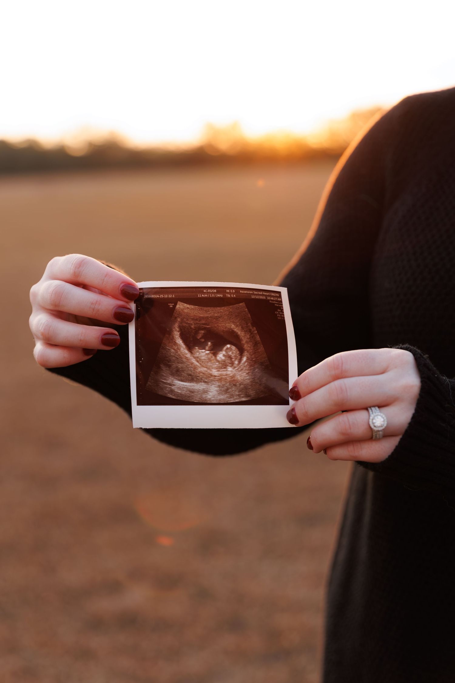 Hands hold ultrasound photos against sunset backdrop in an open field.