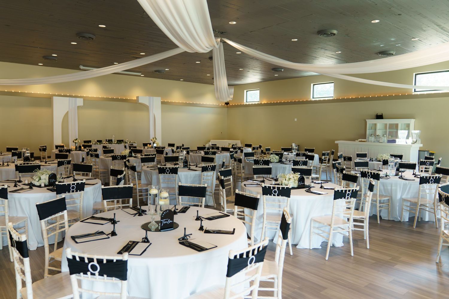 Large banquet hall set up with round tables covered in white linens and black chair covers for an elegant event.
