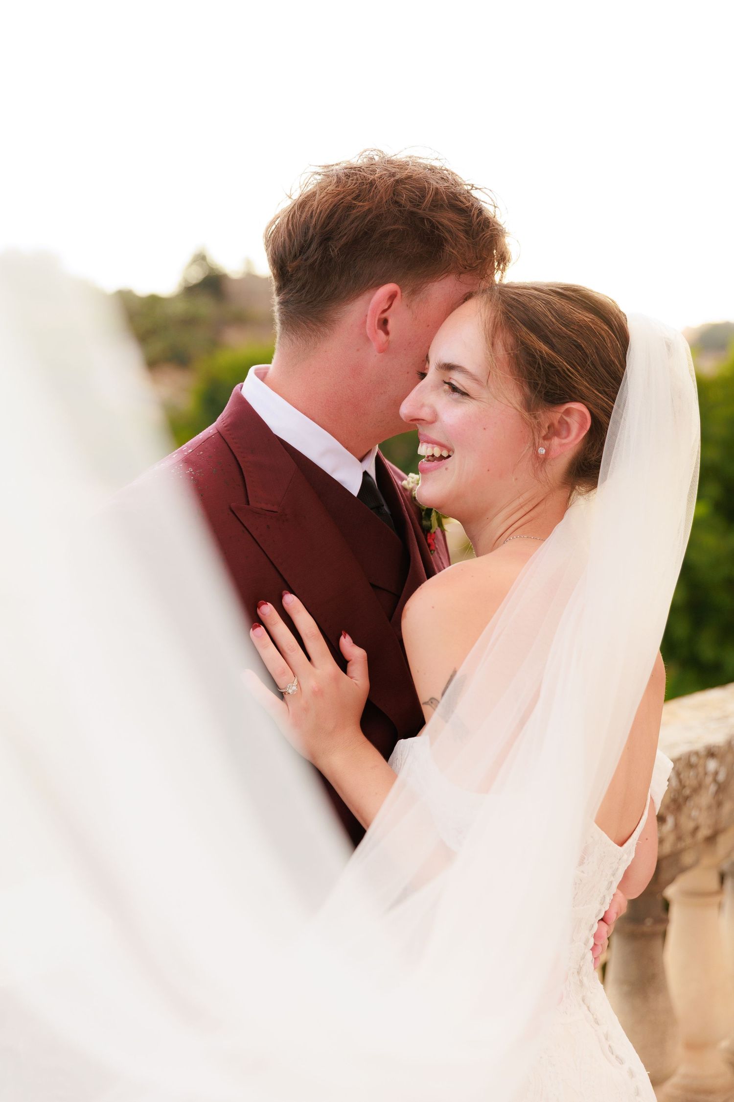 A joyful wedding moment captured on a sunny terrace with a flowing white veil in the breeze.