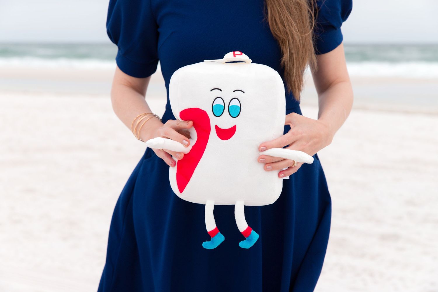 Person in navy dress holding white cat-shaped pregnancy announcement prop on beach.