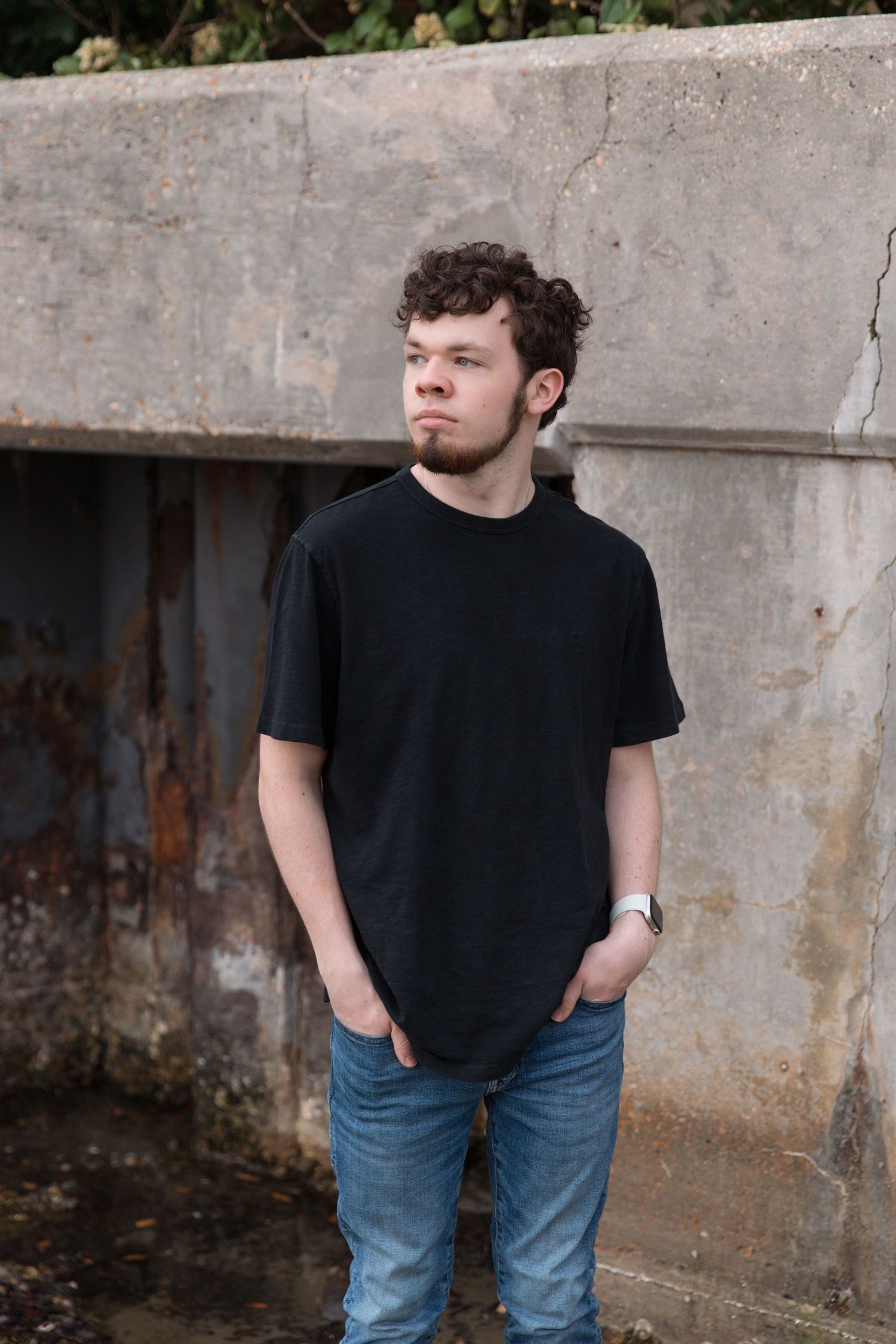 Casual pose against concrete wall wearing black t-shirt and jeans.