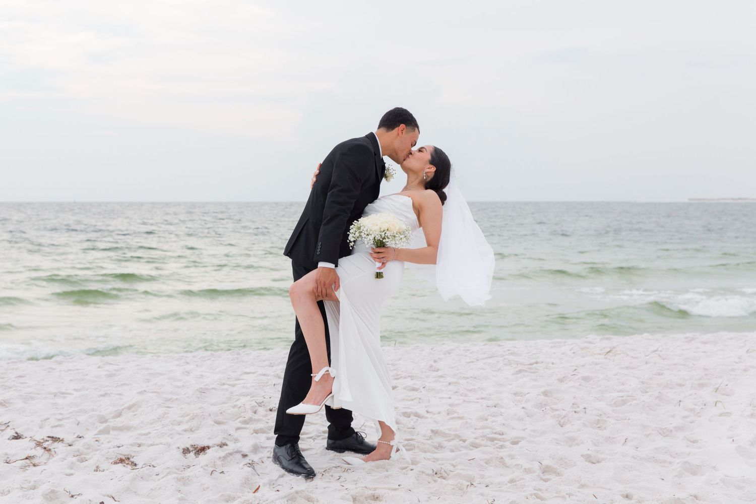 Groom dips bride during romantic beach wedding photo session.