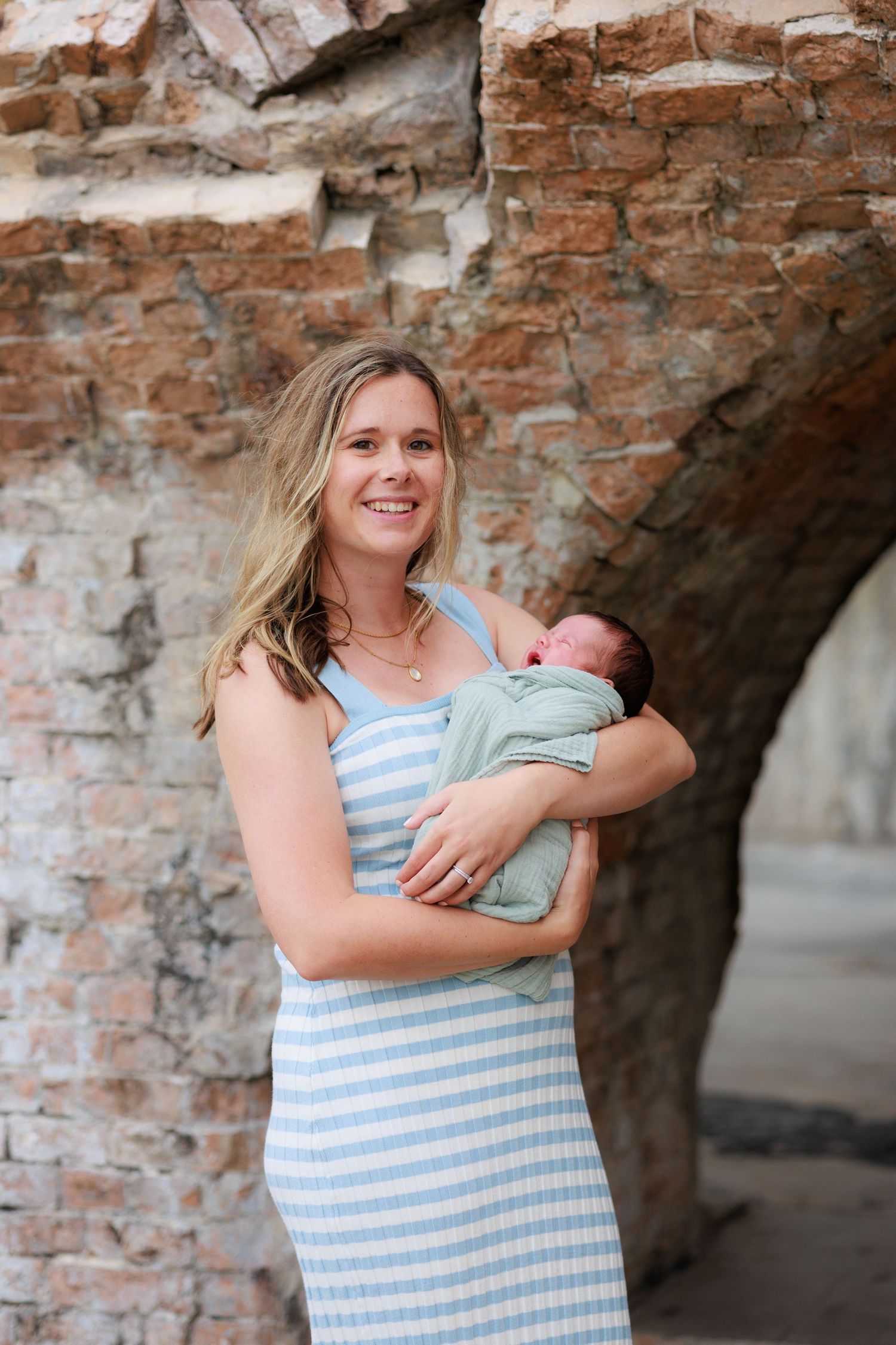 A tender moment captured in a brick archway setting showing nurturing care for a newborn baby.