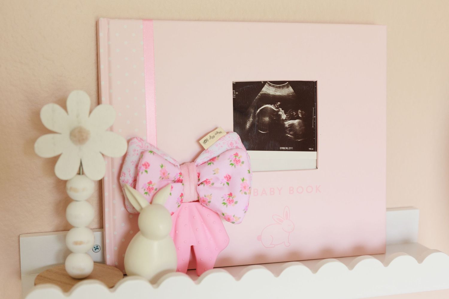 Pink and white baby nursery decor features floral wall art and delicate bows in a soft pastel color scheme.