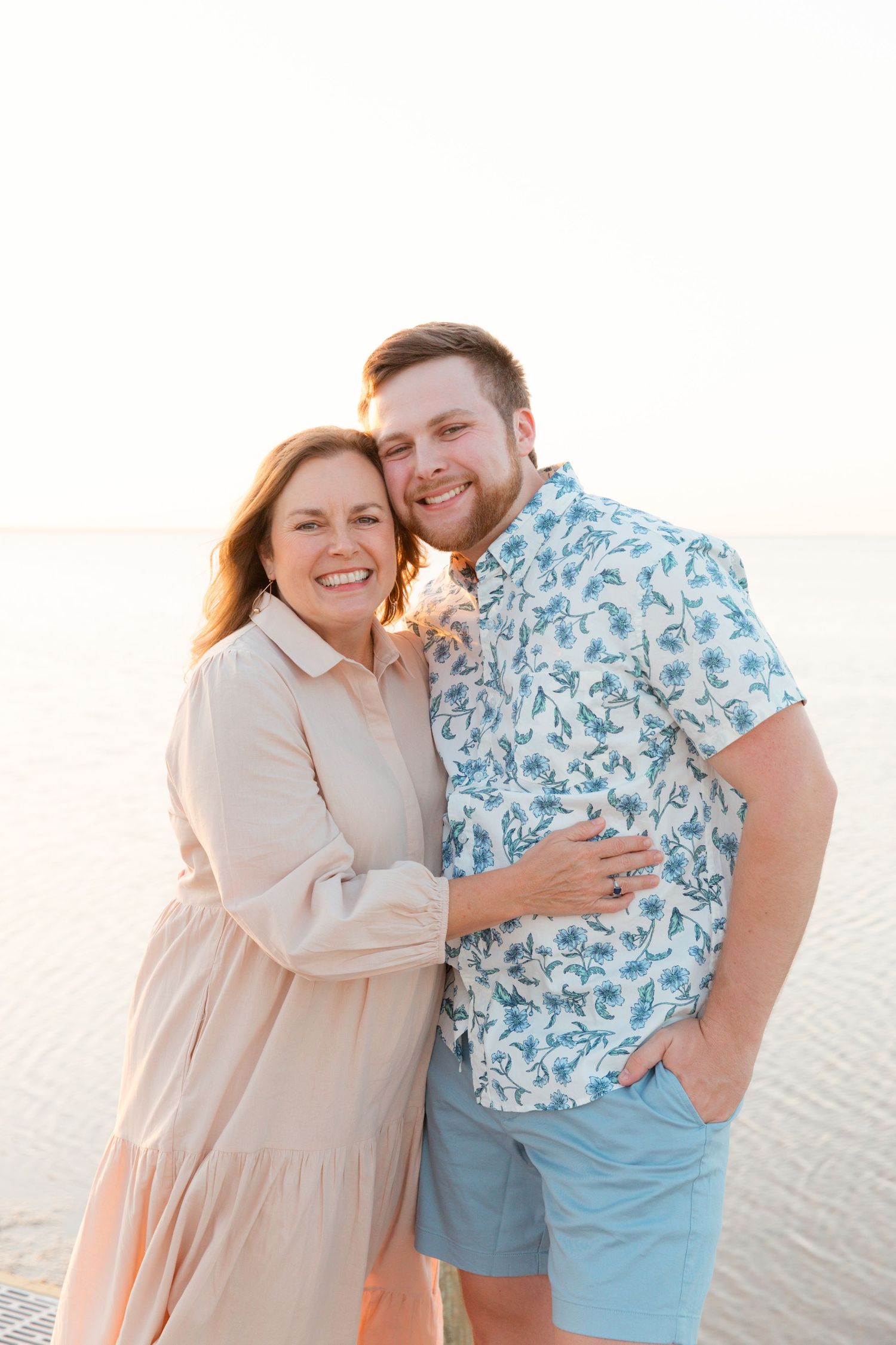 A couple shares a tender moment together on a bright sandy beach at sunset.