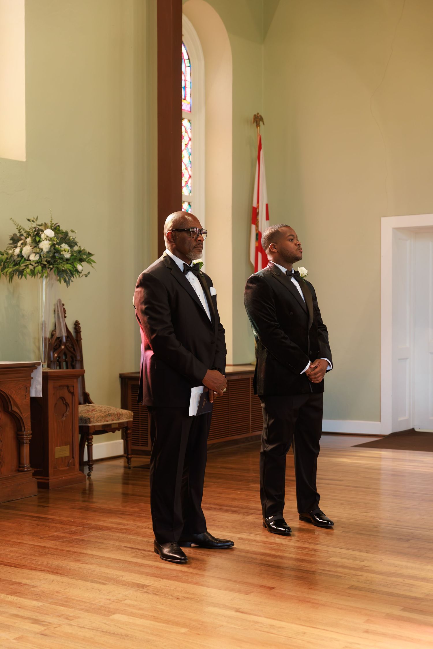 Groomsmen in black tuxedos stand in formation at the front of an elegant church sanctuary.