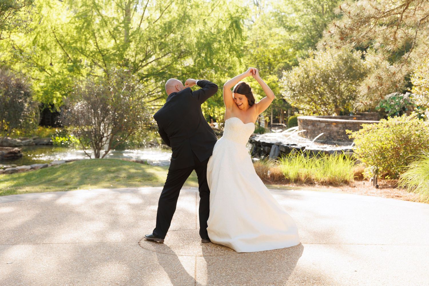 Couple dancing outdoors as groom spins bride in white wedding dress in a lush garden.