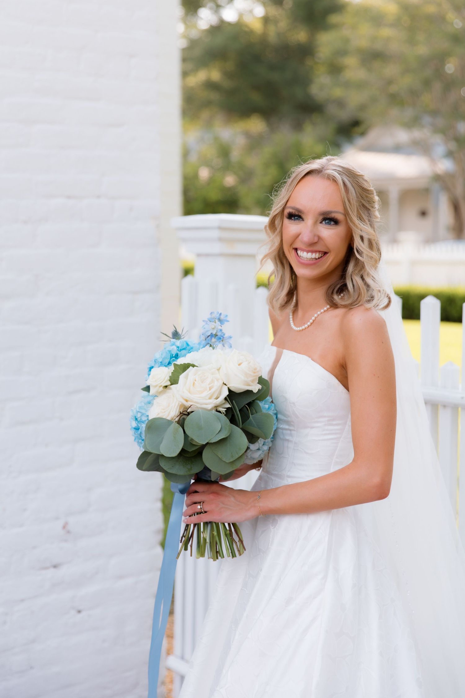 Radiant bride in strapless gown holds bouquet with blue hydrangeas and white roses.