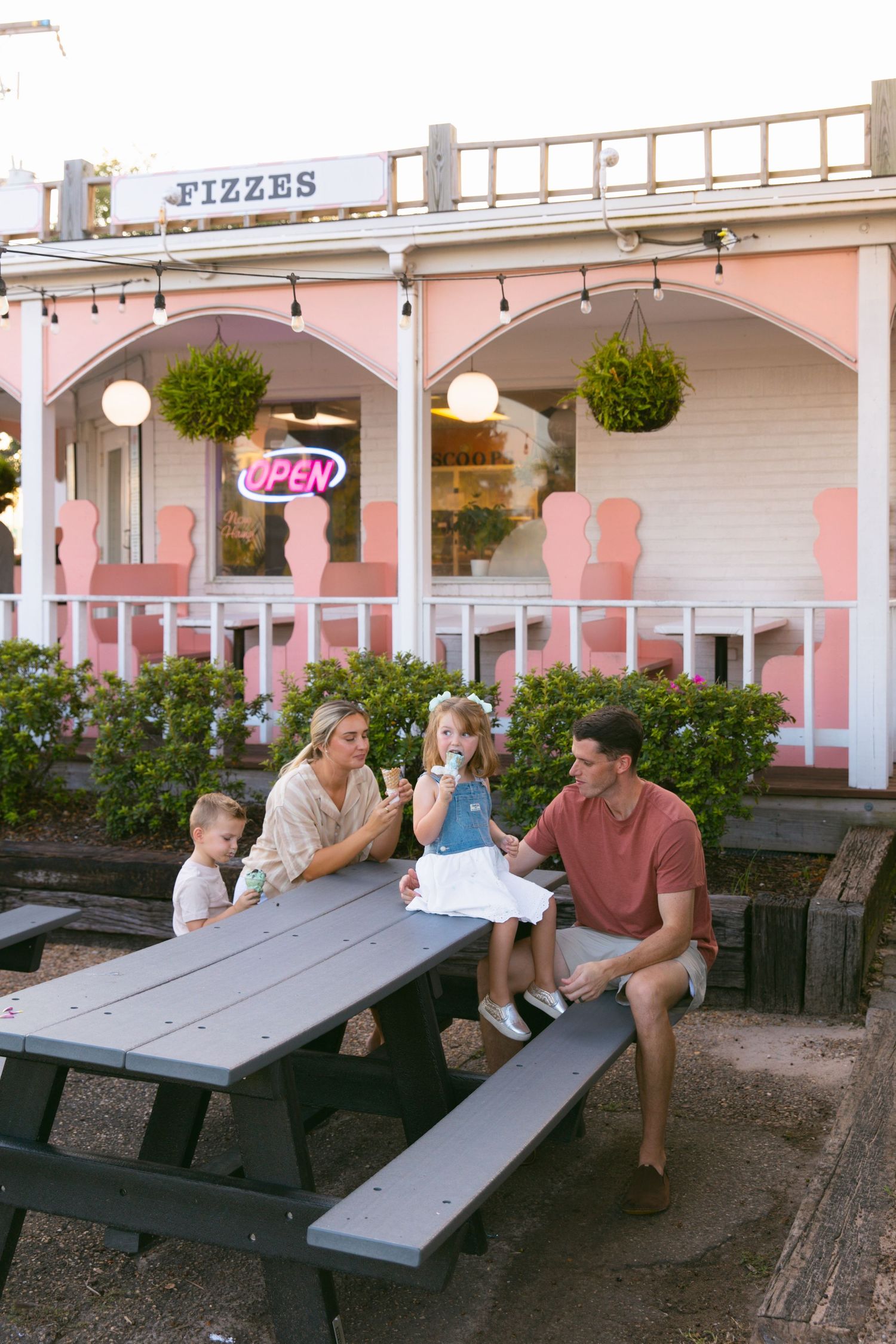 Family enjoying time together at a pink-colored ice cream parlor with outdoor seating.