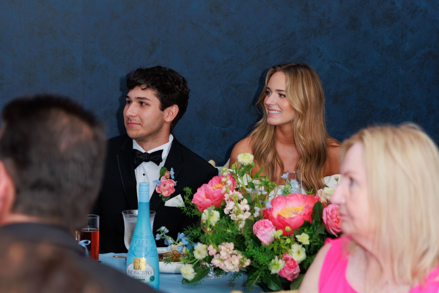 Elegant reception dinner table decorated with pink and white floral centerpieces and glowing blue uplighting.