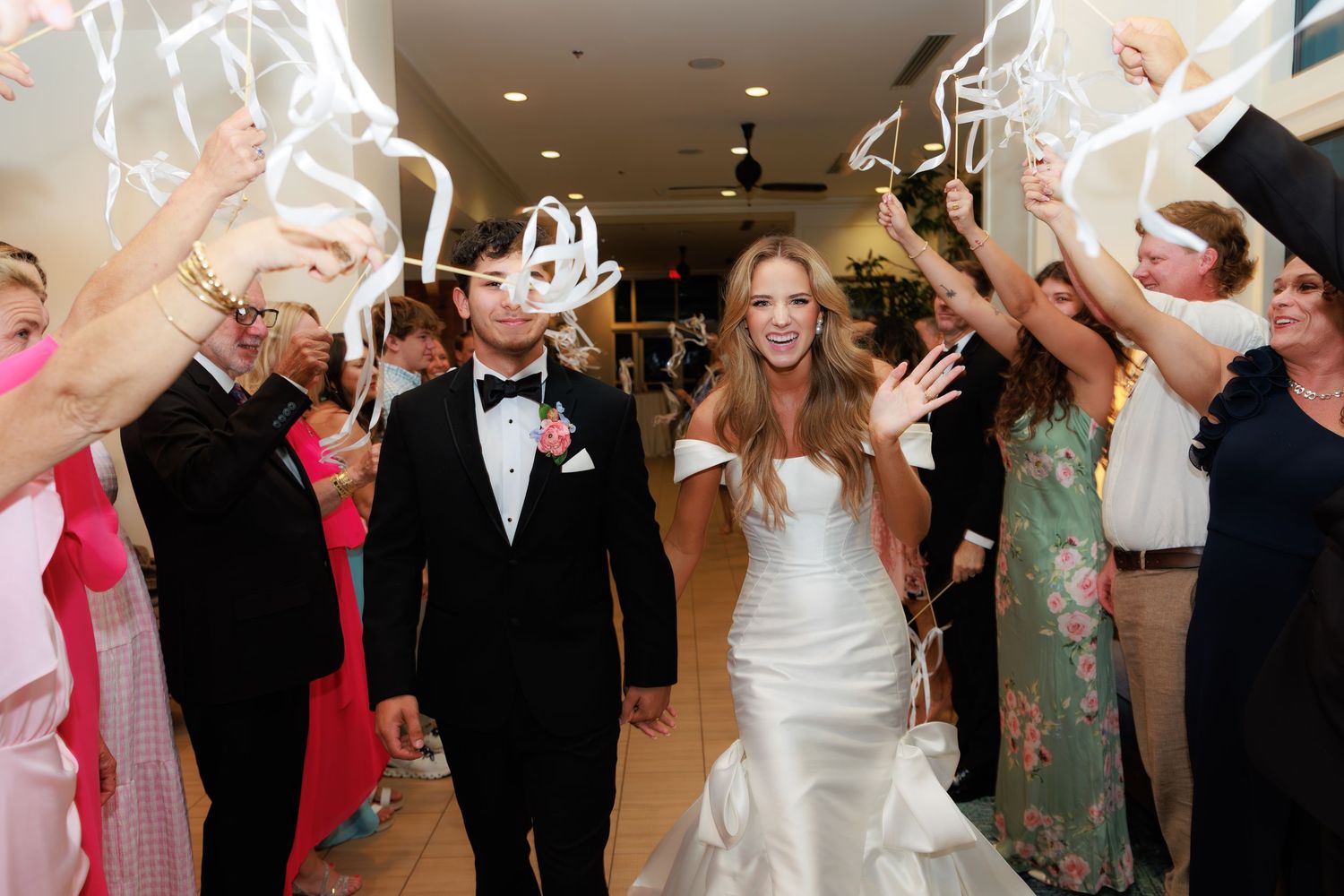 Wedding couple exits their reception venue through a tunnel of guests waving sparklers in celebration.
