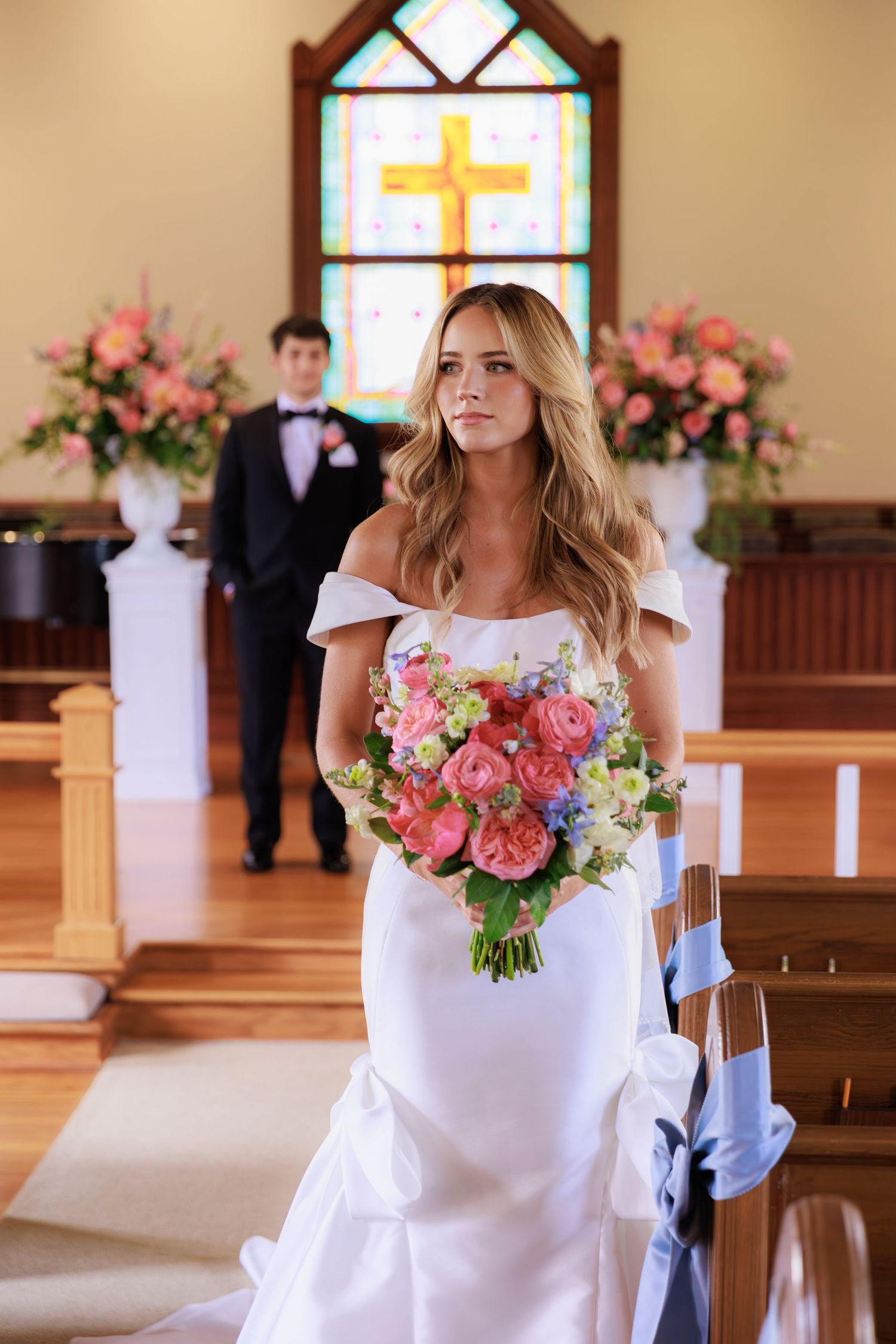 A stylish white wedding dress with colorful coral and pink flower bouquet in a church setting.