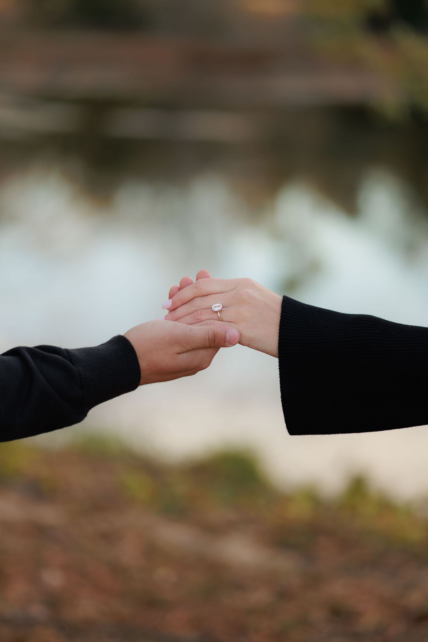 A close-up view of hands reaching out and touching each other in a romantic gesture against a blurred background.