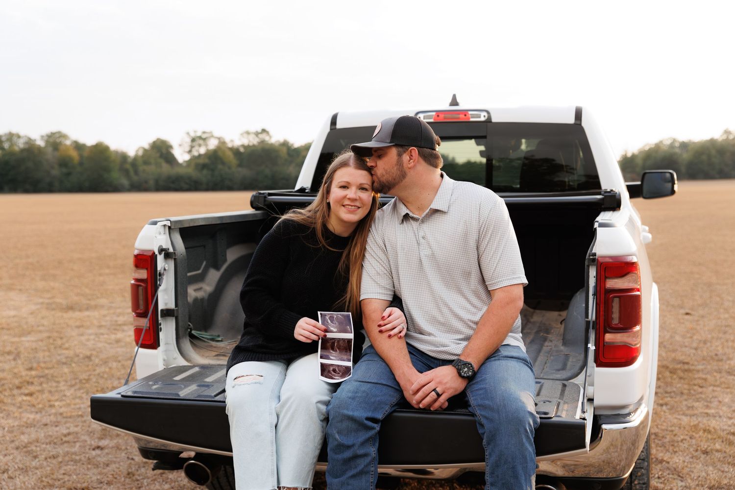 Couple sitting together on a pickup truck tailgate in a rustic outdoor setting at sunset.