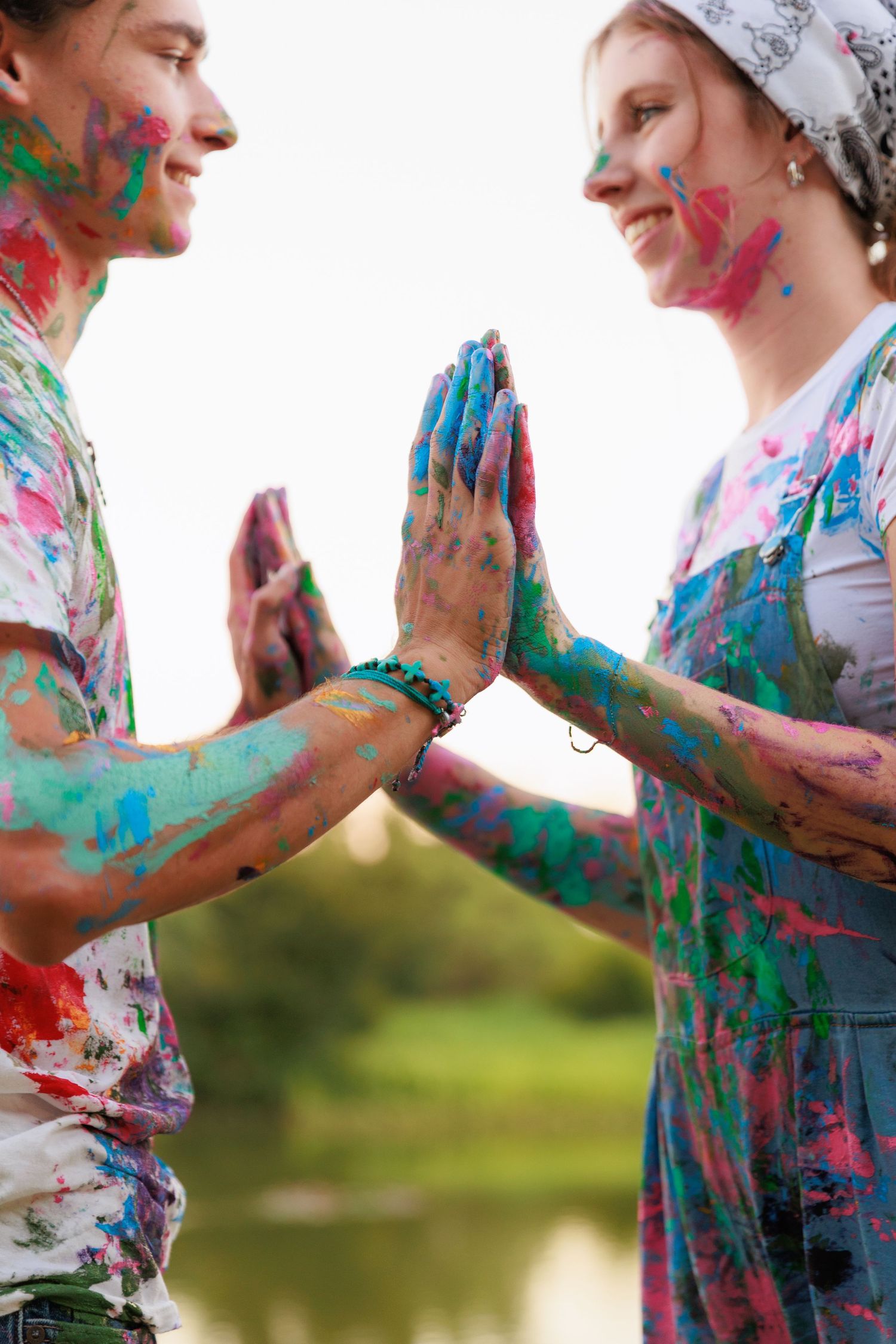 Couple covered in colorful powder paint playfully interact during an outdoor photoshoot by a lake.
