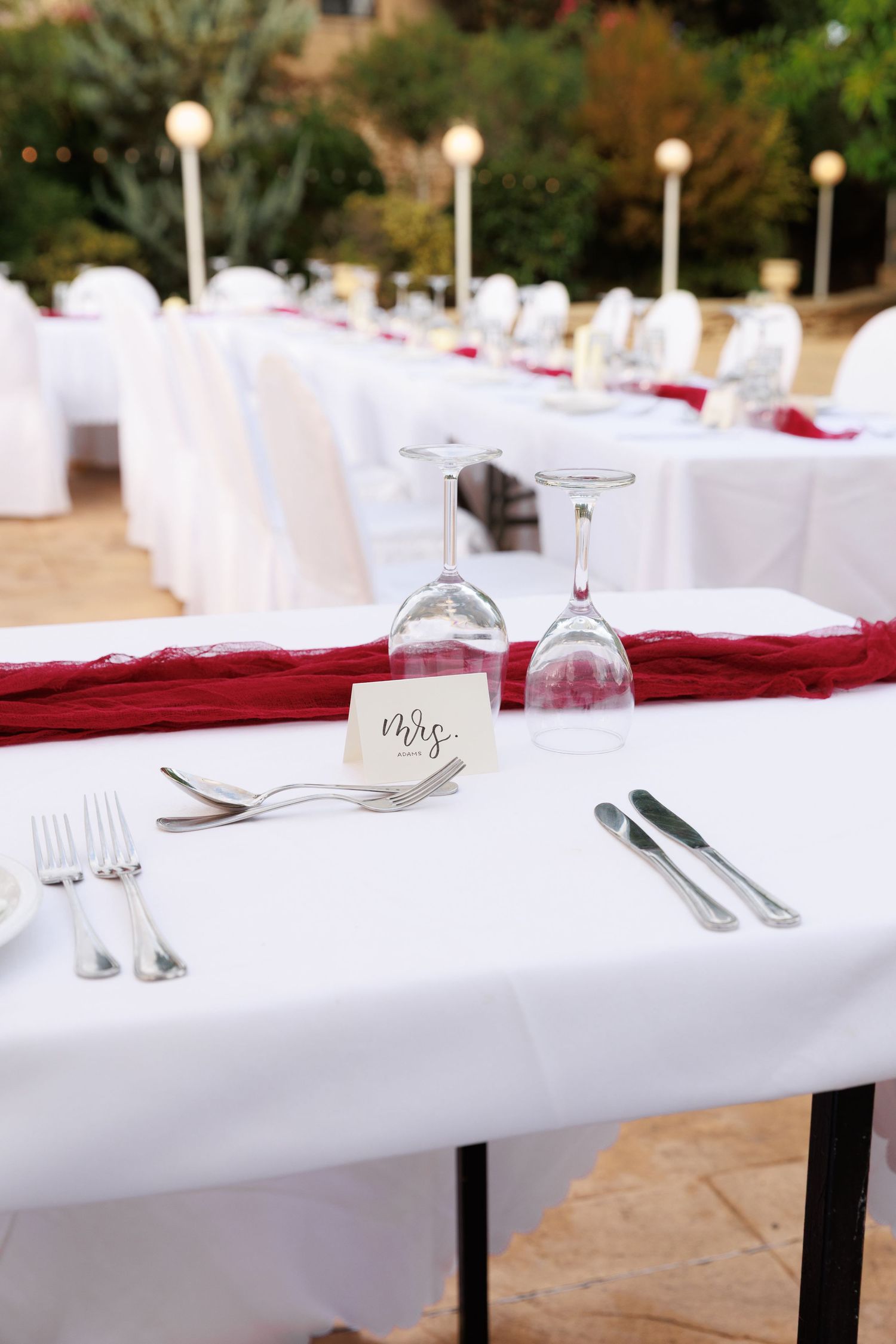 White tablecloth dining setup with red accents and glassware arranged for an elegant outdoor event.