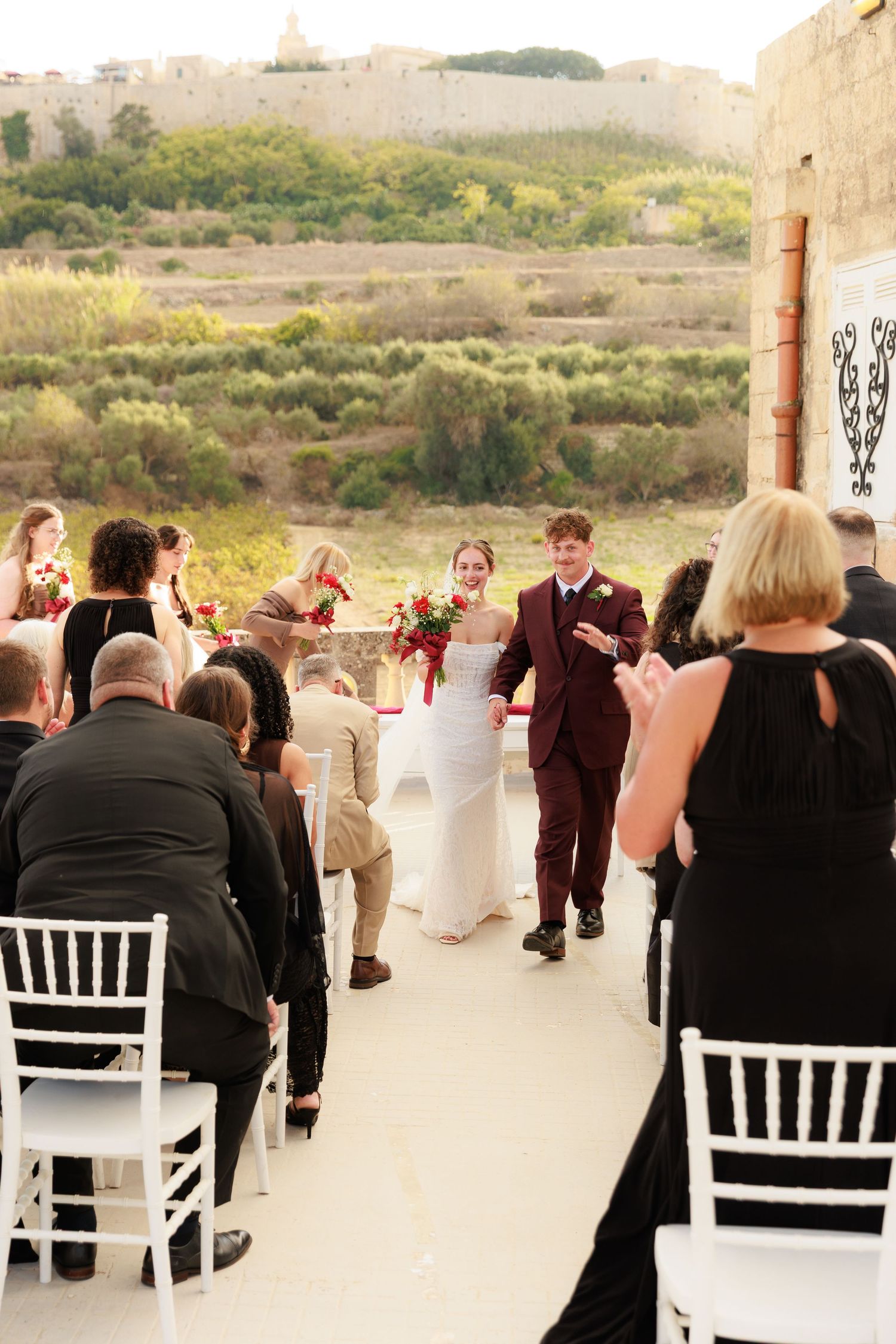 Guests seated in white chairs at an outdoor wedding ceremony with scenic natural landscape in the background.