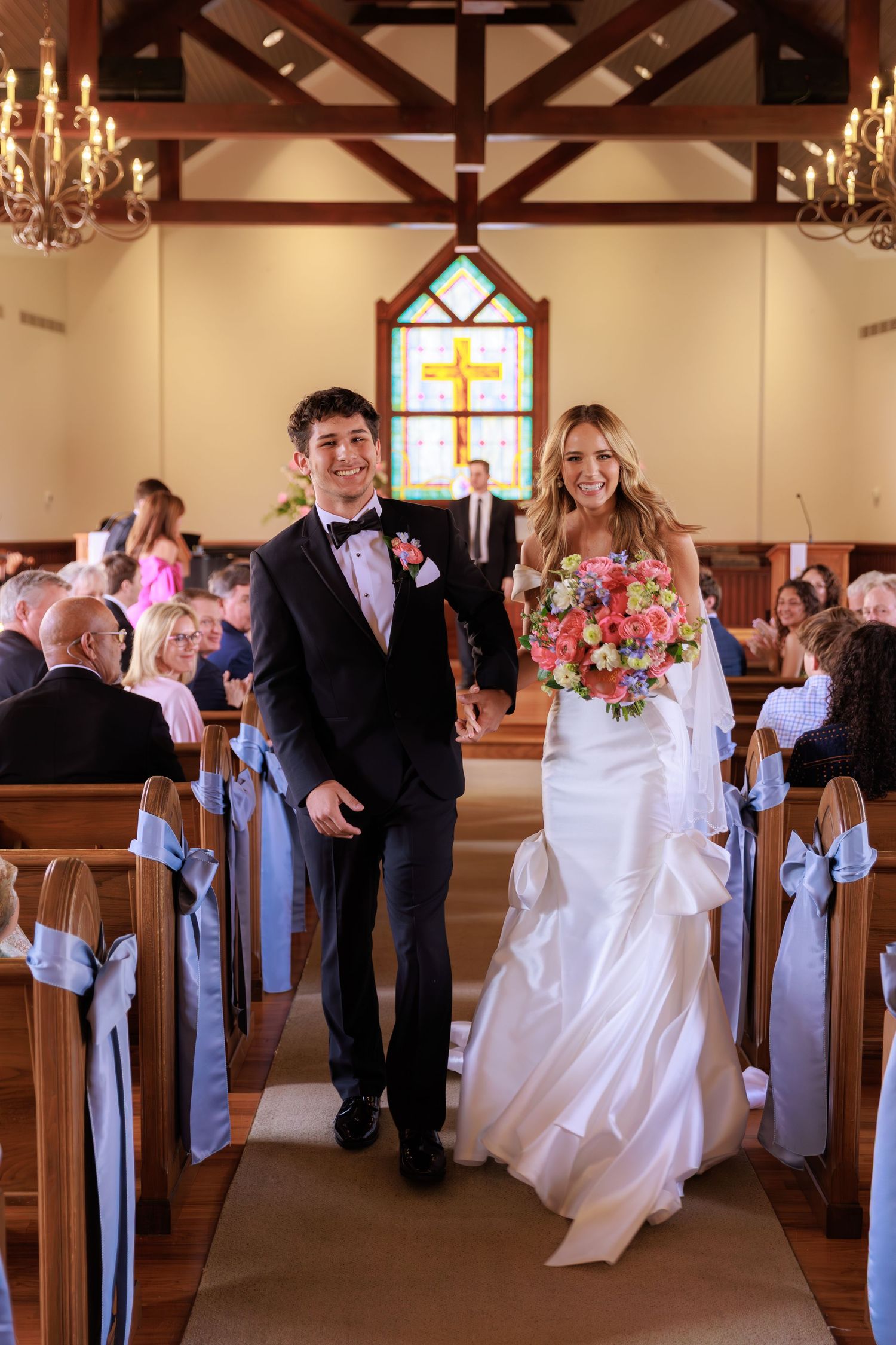 A wedding processional with couples walking down the church aisle decorated with light blue bows and flowers.