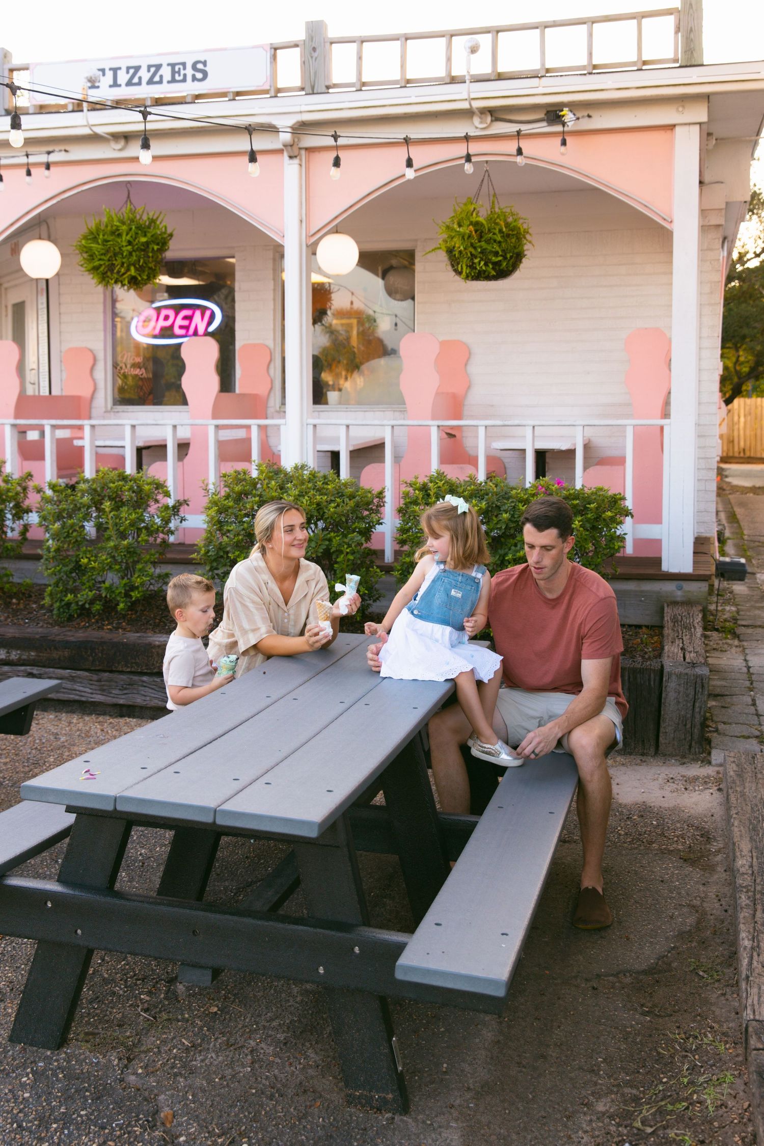 A family enjoys ice cream while sitting at picnic tables outside a retro pink and white ice cream shop.