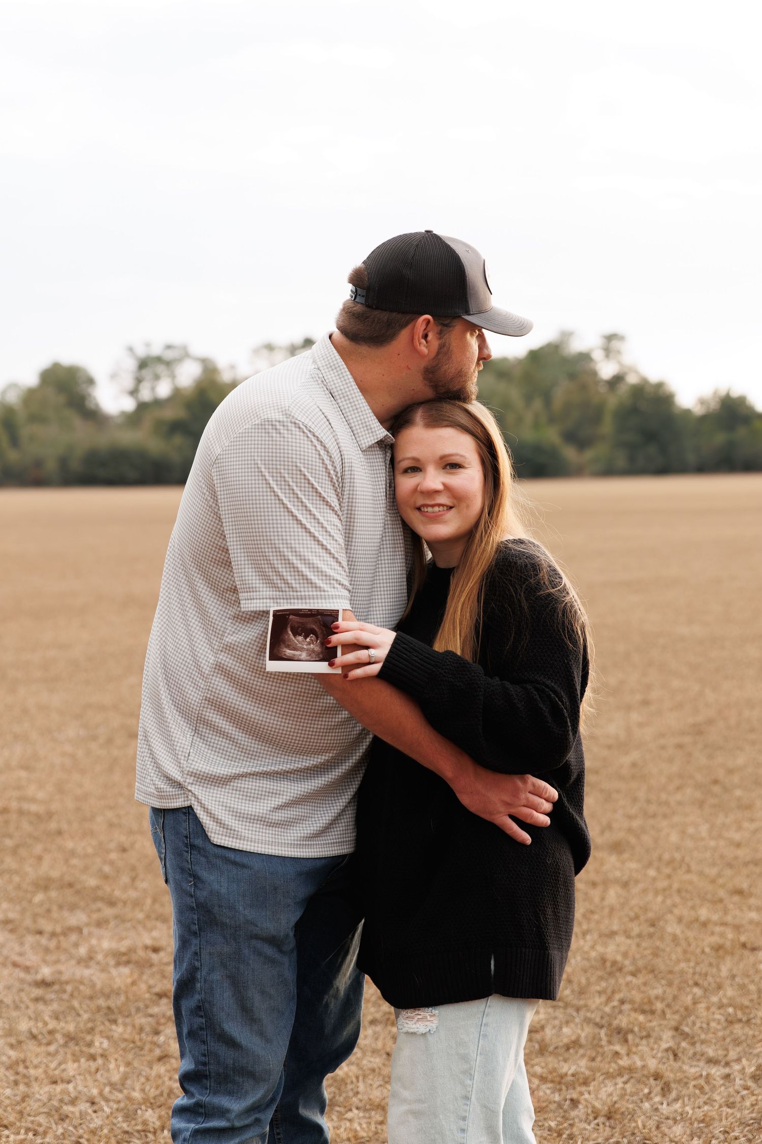A couple shares tender moments while holding a photo in a rustic outdoor setting.