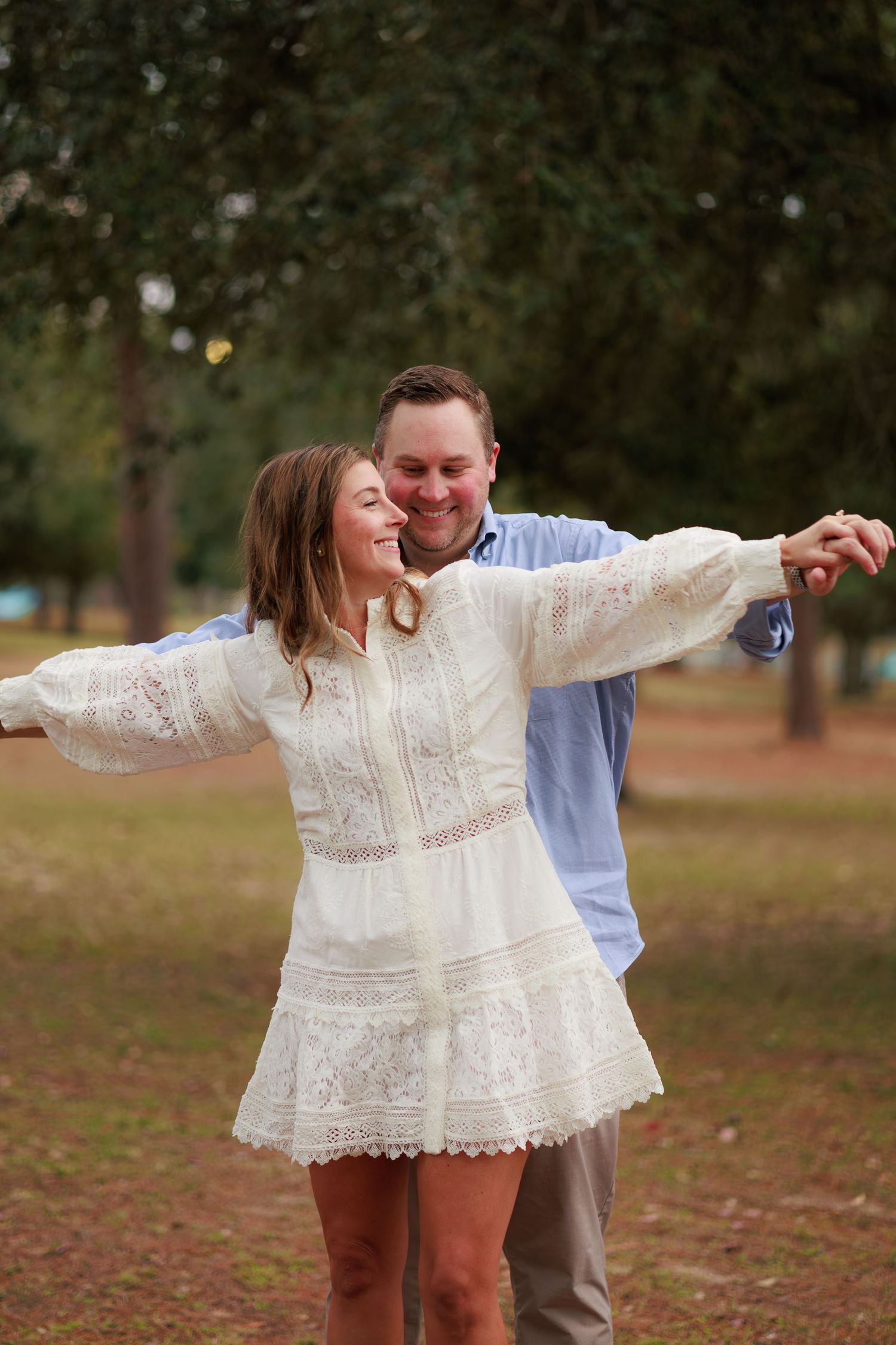 A couple dances joyfully outdoors surrounded by fall foliage and natural scenery.