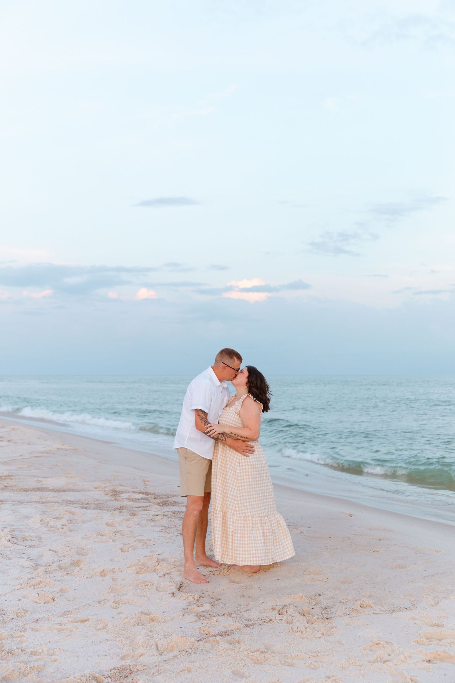 Romantic beach photoshoot at sunset with soft pastel sky and ocean backdrop.