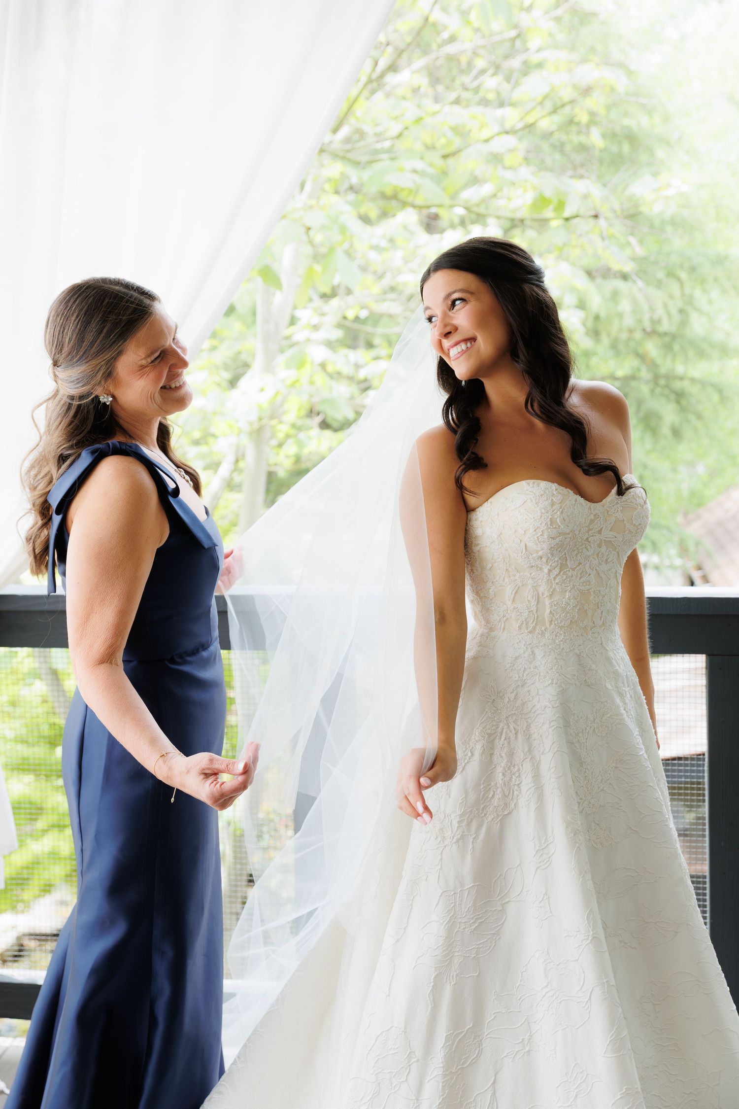 Bride in strapless lace gown shares a joyful moment with her mother in a navy dress before the wedding.