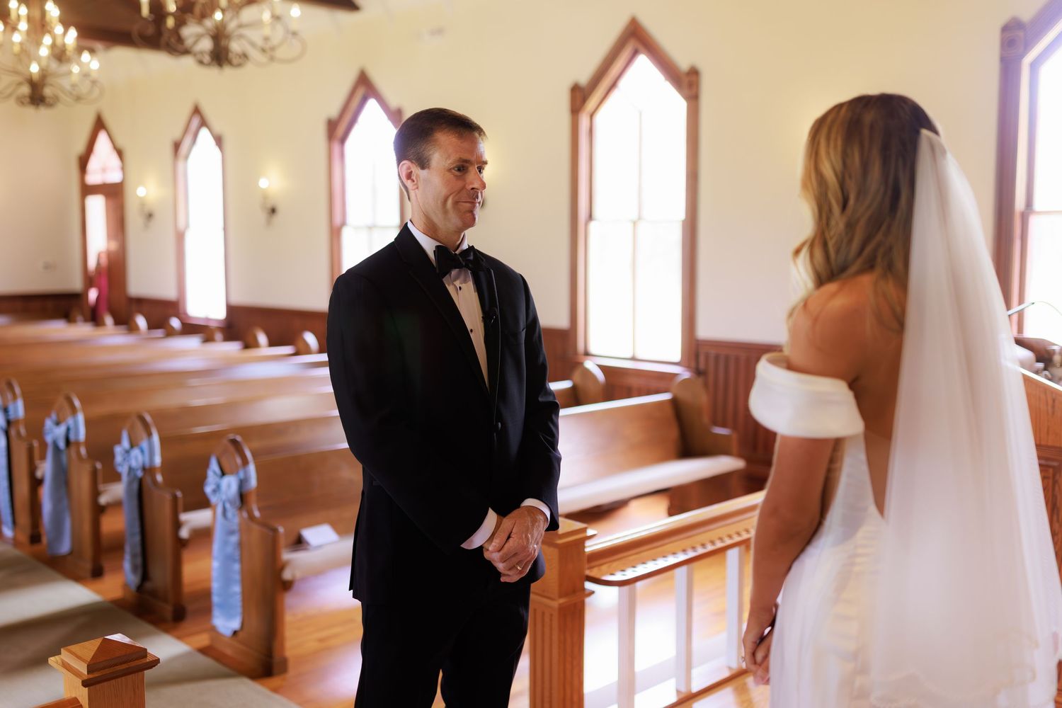 A bride and groom share an intimate moment in a charming chapel with gothic windows and wooden pews.