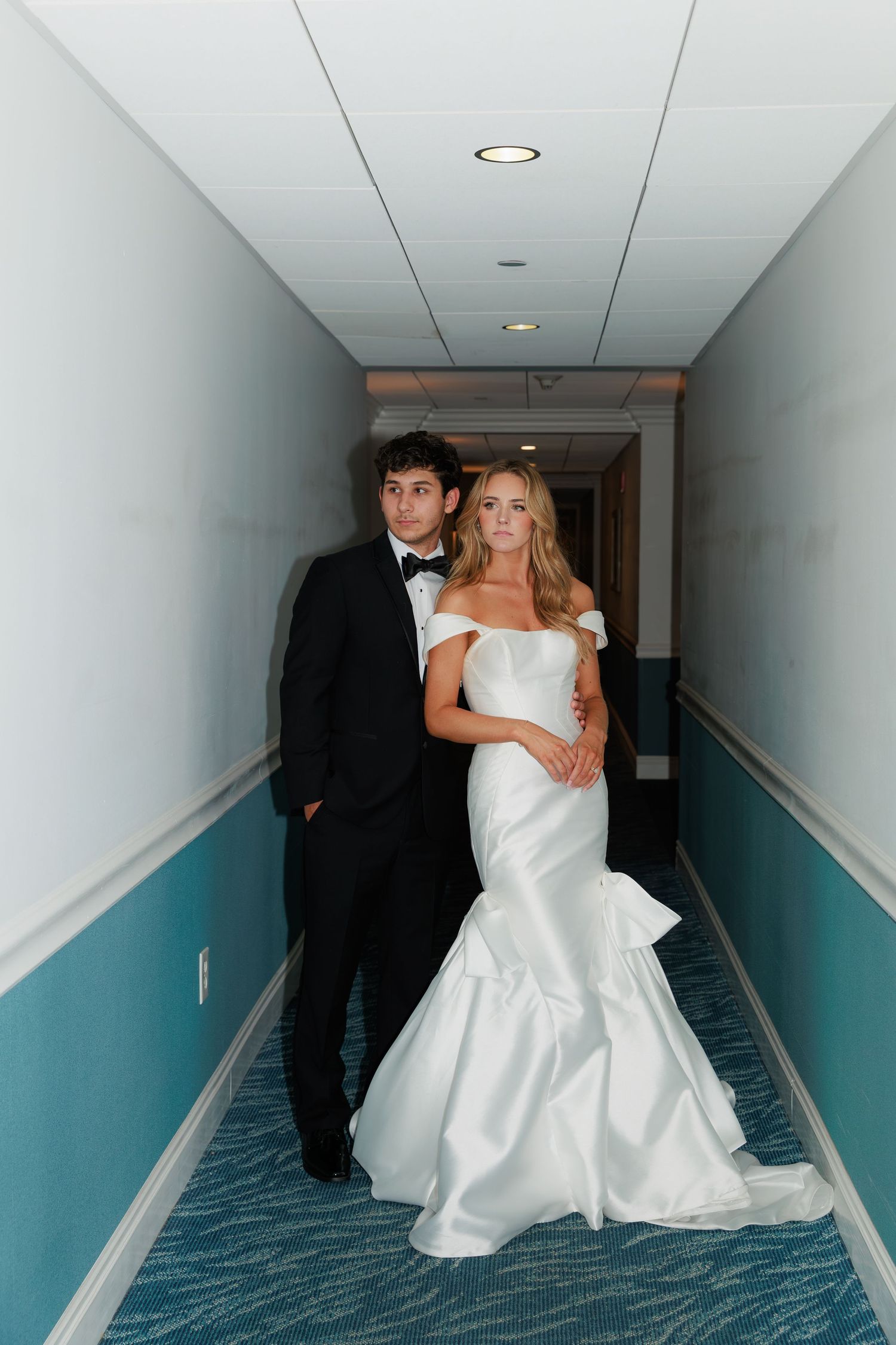 Wedding couple walking through hotel hallway with blue and white walls.