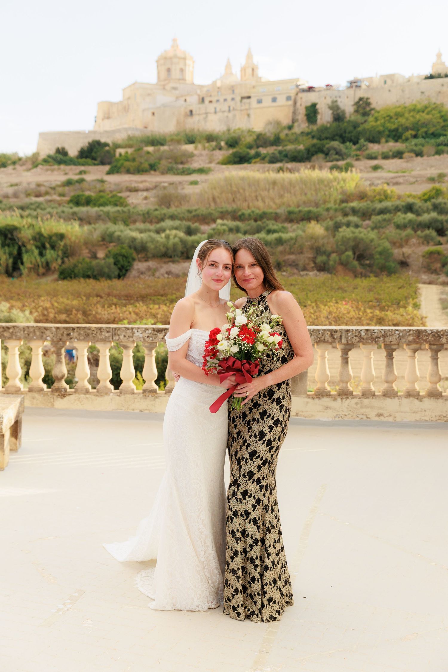 Wedding photos taken at scenic overlook with stone balustrade and historic buildings on hilltop in background.