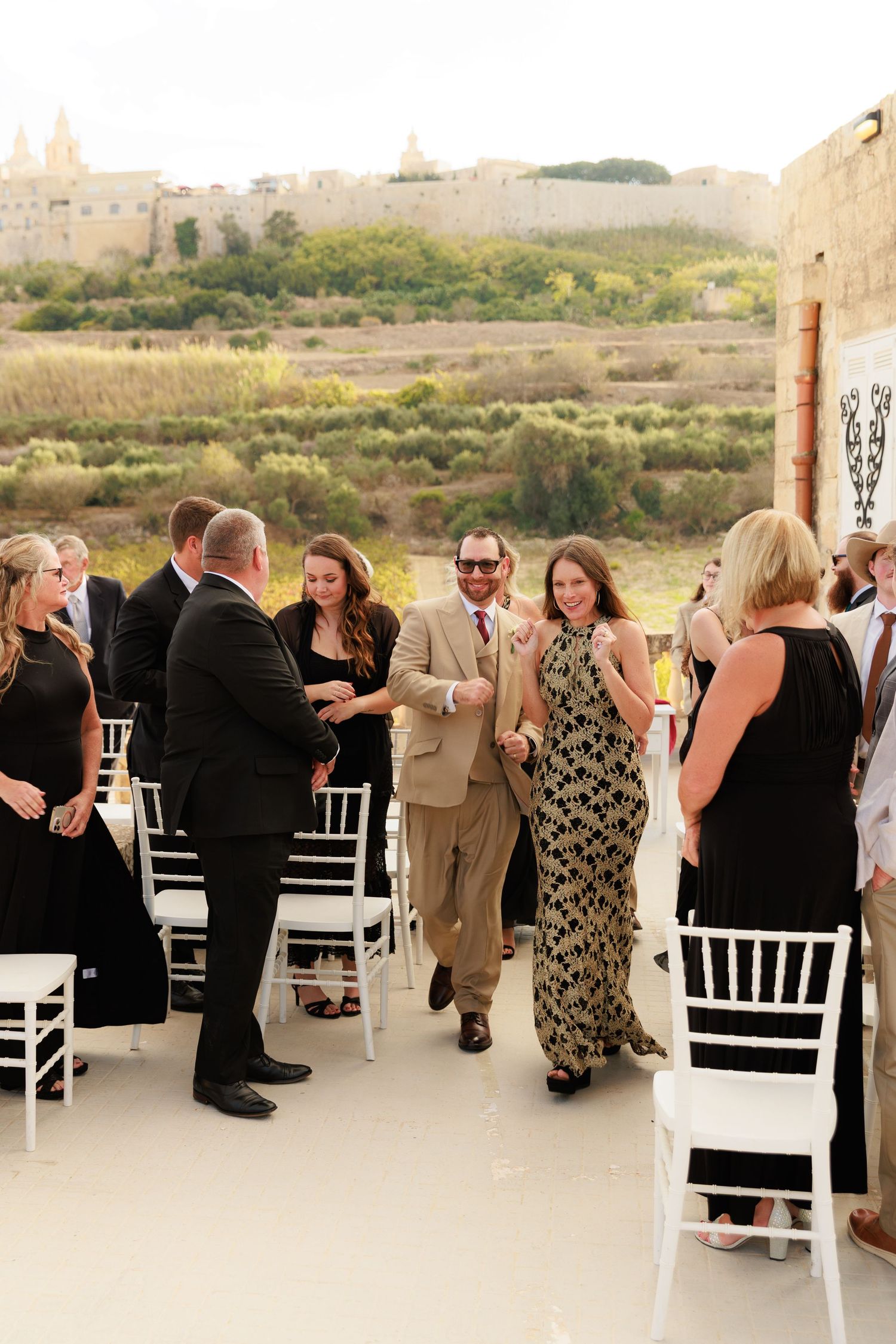 Wedding celebration continues with guests mingling and dancing on an outdoor terrace overlooking a scenic landscape.