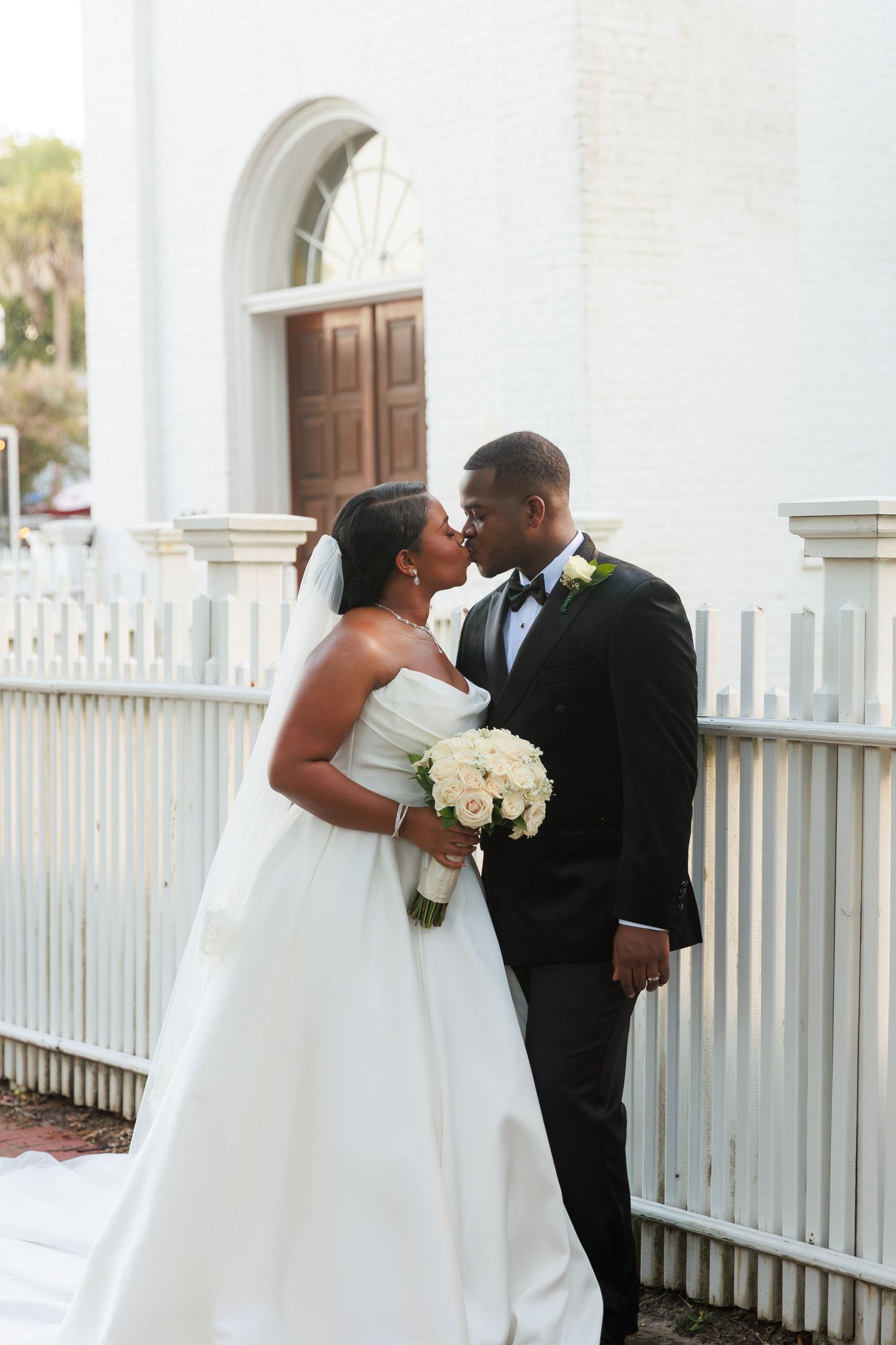 Wedding couple embraces and shares tender moments against a white building backdrop.