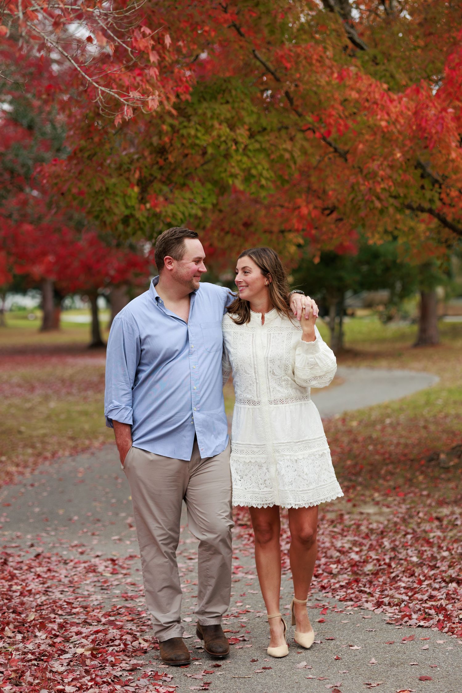 A couple walks together on a path surrounded by vibrant red fall foliage and autumn leaves.