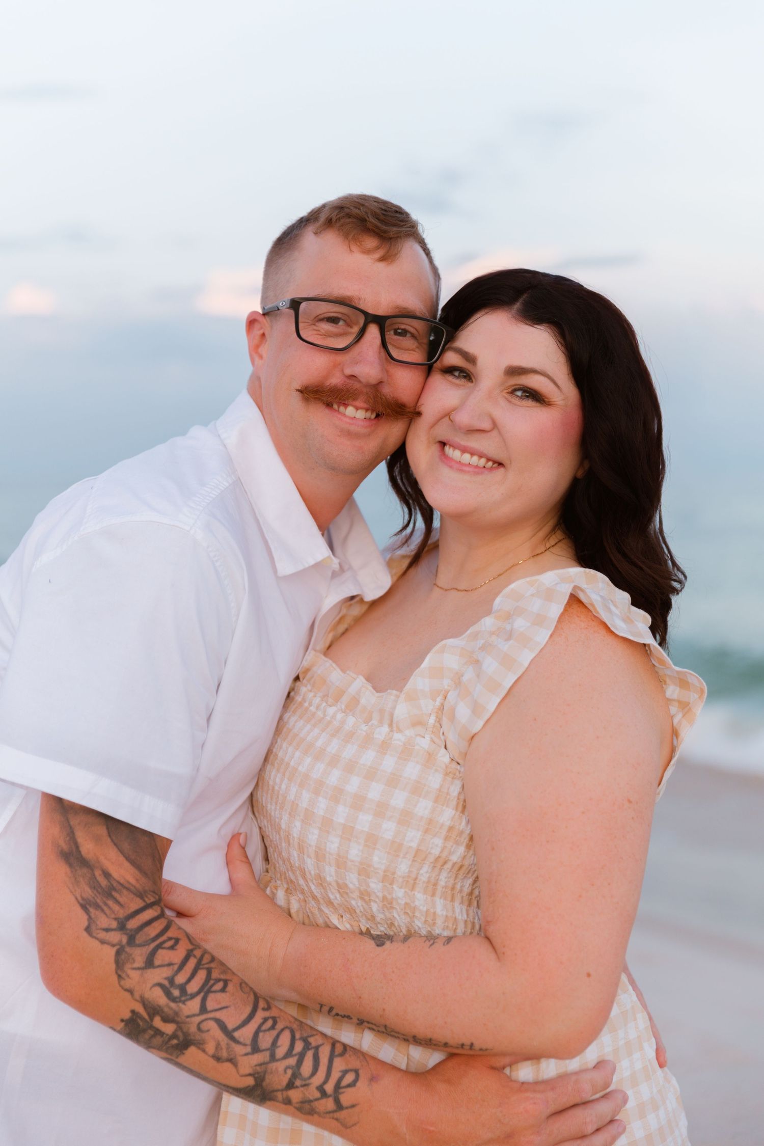 Couple embracing on the beach at sunset with ocean waves in the background.