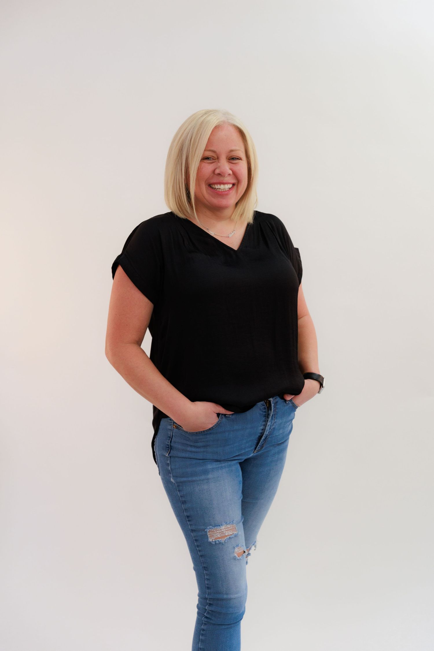 Casual studio portrait in black v-neck top and distressed jeans against white background.
