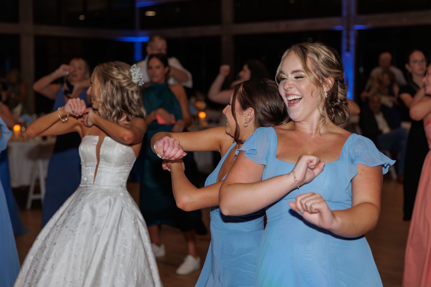 Wedding party dancing and laughing together in coordinated blue bridesmaid dresses.